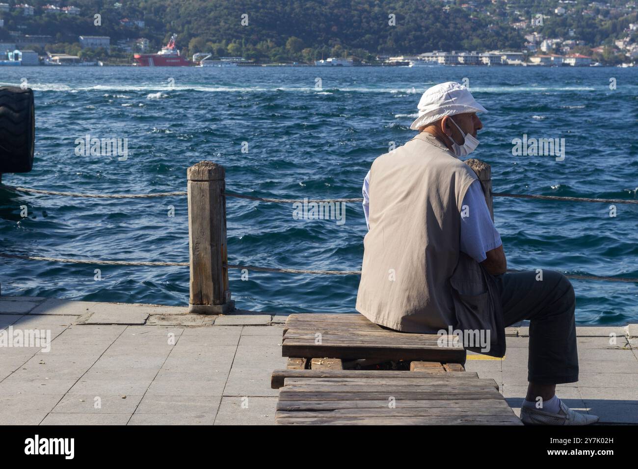 Plan vertical d'un homme dans un masque médical se reposant sur un panneau de bois sur les quais d'Istanbul, Turquie Banque D'Images