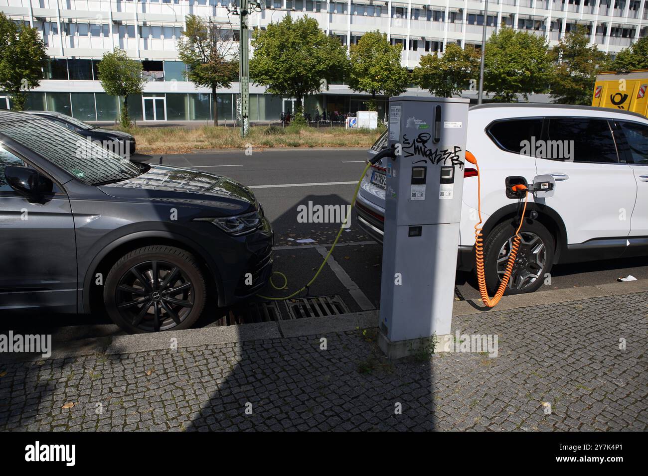 Deux voitures électriques étant chargées avec des câbles branchés, les câbles sont branchés à un chargeur public de rue installé sur un trottoir berlinois Banque D'Images
