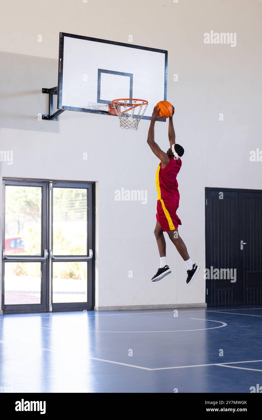 Basket-ball trempé, athlète en uniforme rouge sautant haut dans un court couvert, espace copie Banque D'Images