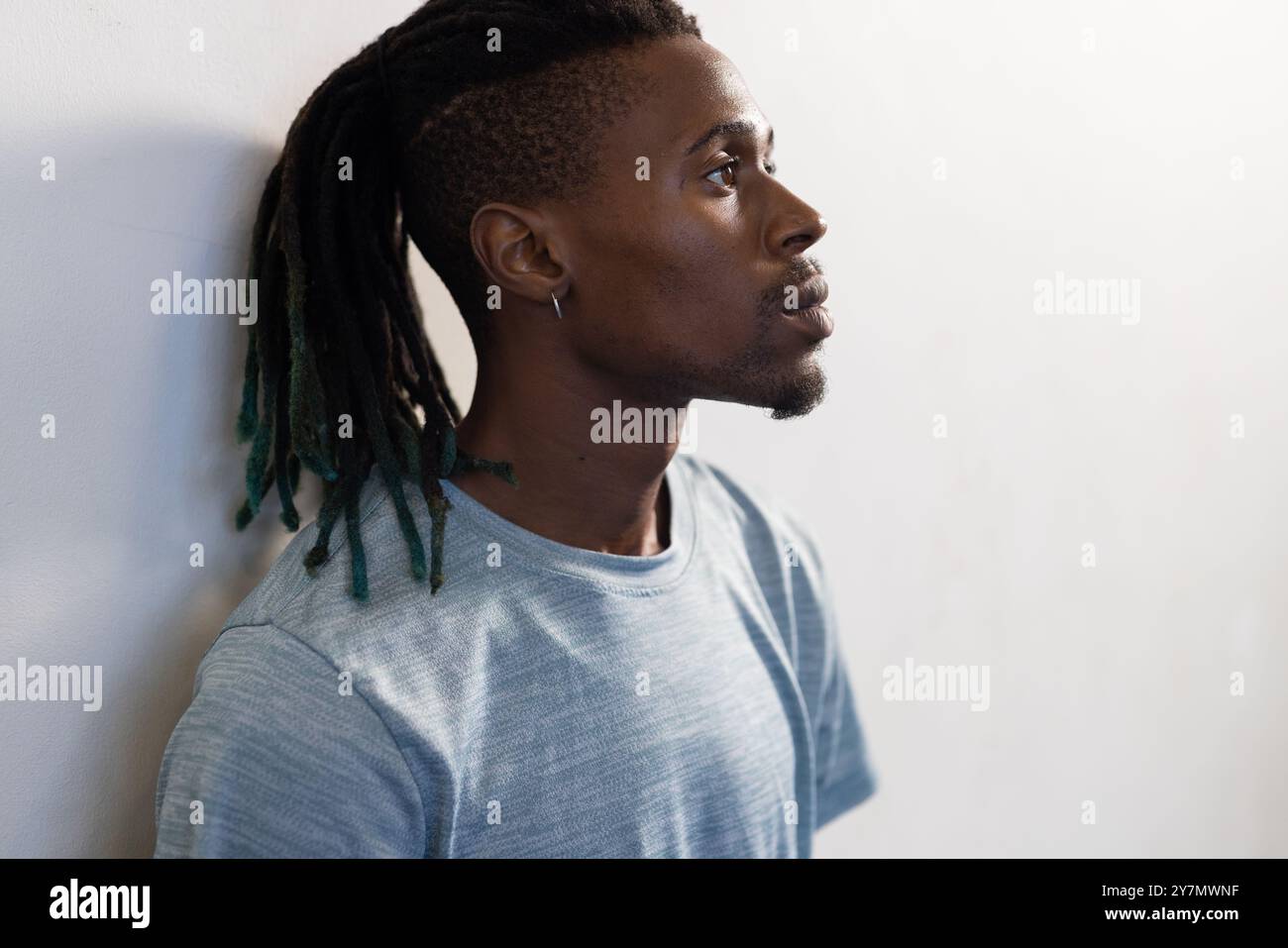 Profil de l'homme avec des dreadlocks regardant réfléchi, portant une chemise bleue décontractée Banque D'Images