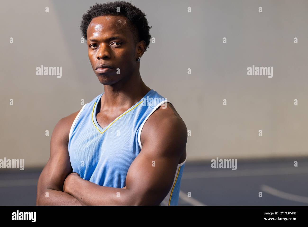 Joueur de basket-ball afro-américain en maillot bleu debout avec les bras croisés sur le terrain Banque D'Images