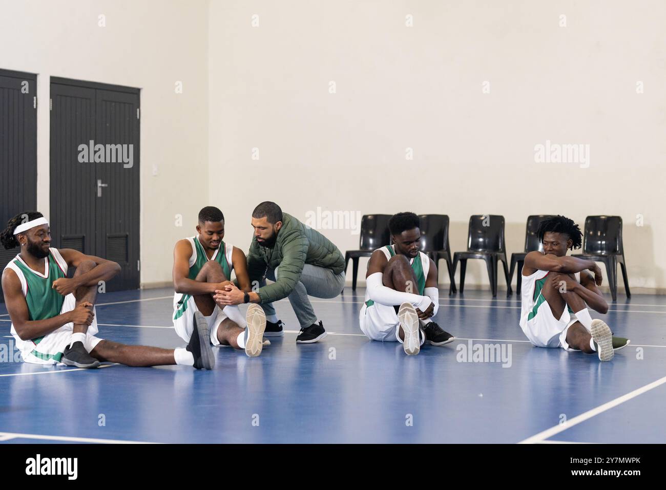 Entraîneur de basket-ball aidant les joueurs à s'étirer sur le terrain pendant la séance d'entraînement Banque D'Images