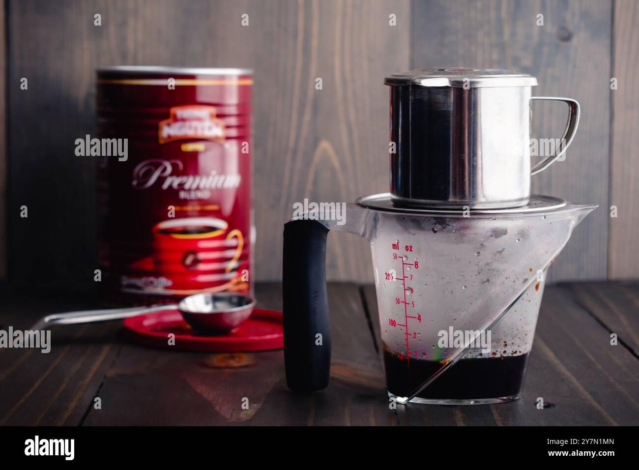 Préparation du café vietnamien avec un Phin sur une tasse à mesurer : café fort qui coule d'un filtre phin avec une boîte de café en arrière-plan Banque D'Images