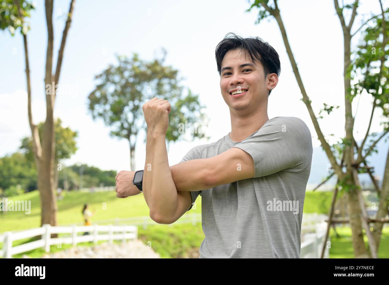 Un homme asiatique beau, en forme et en bonne santé en vêtements de sport étire son bras, s'échauffe avant de courir dans un parc par une journée lumineuse. personnes et concepts sportifs Banque D'Images