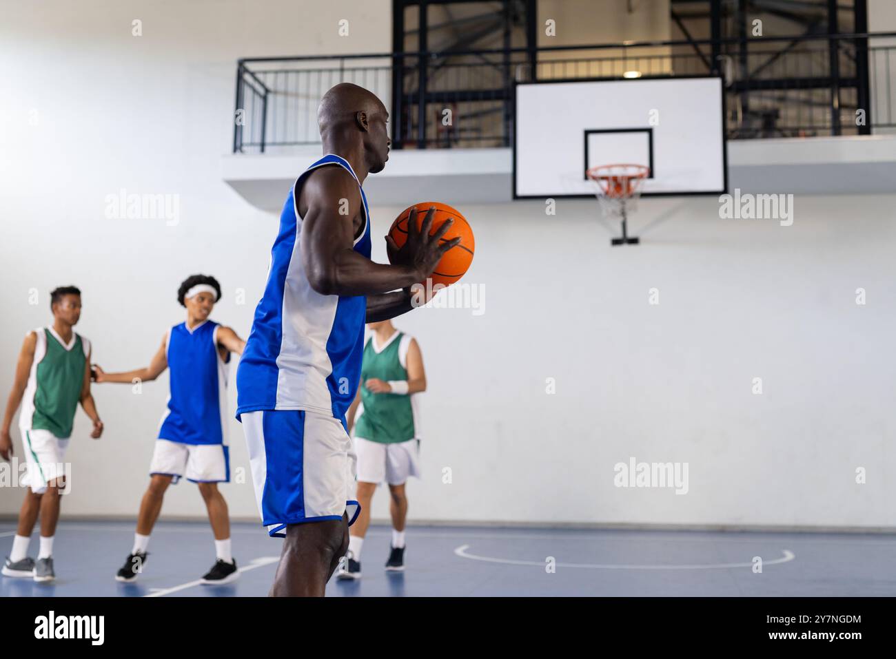 Jouer au basket-ball, homme tenant le ballon tandis que les coéquipiers se préparent en arrière-plan Banque D'Images