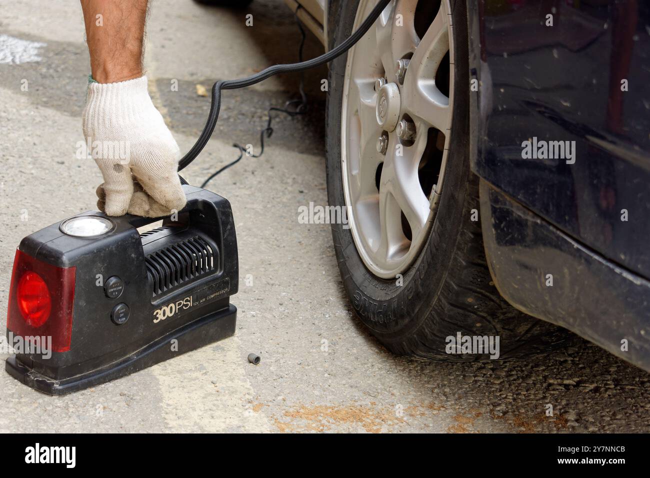 Une personne en gant blanc gonfle pneu de voiture avec compresseur d'air portable sur la rue urbaine. Le compresseur est noir avec une lumière rouge. Voiture est berline noire avec si Banque D'Images