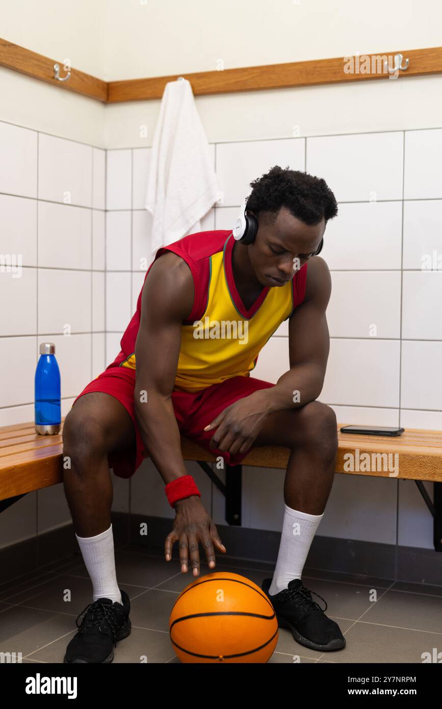 Écouter de la musique avec des écouteurs, joueur de basket-ball assis dans le vestiaire Banque D'Images