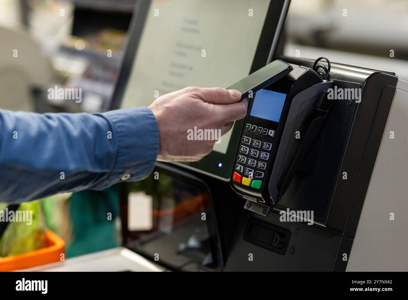 La personne effectue un paiement sans contact en utilisant un smartphone à la caisse du magasin. La technologie permet des transactions pratiques et sécurisées dans un environnement de vente au détail. Concentrez-vous sur la main tenant le téléphone sur le terminal de paiement. Banque D'Images