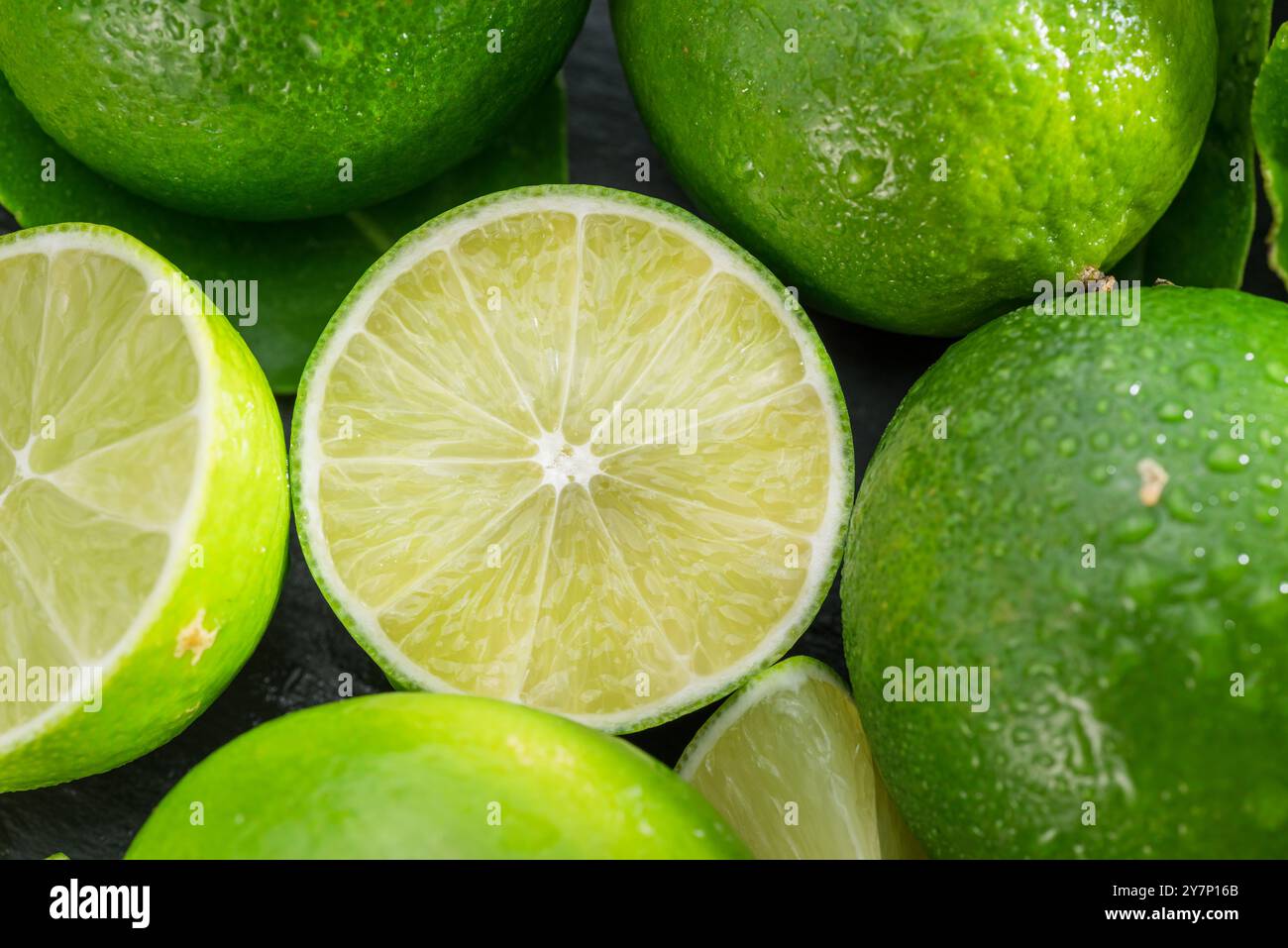 Fruits de citron vert mûrs avec des tranches et des feuilles de citron vert sur une table en pierre grise. Joli fond d'agrumes de fruits pour vos projets. Banque D'Images