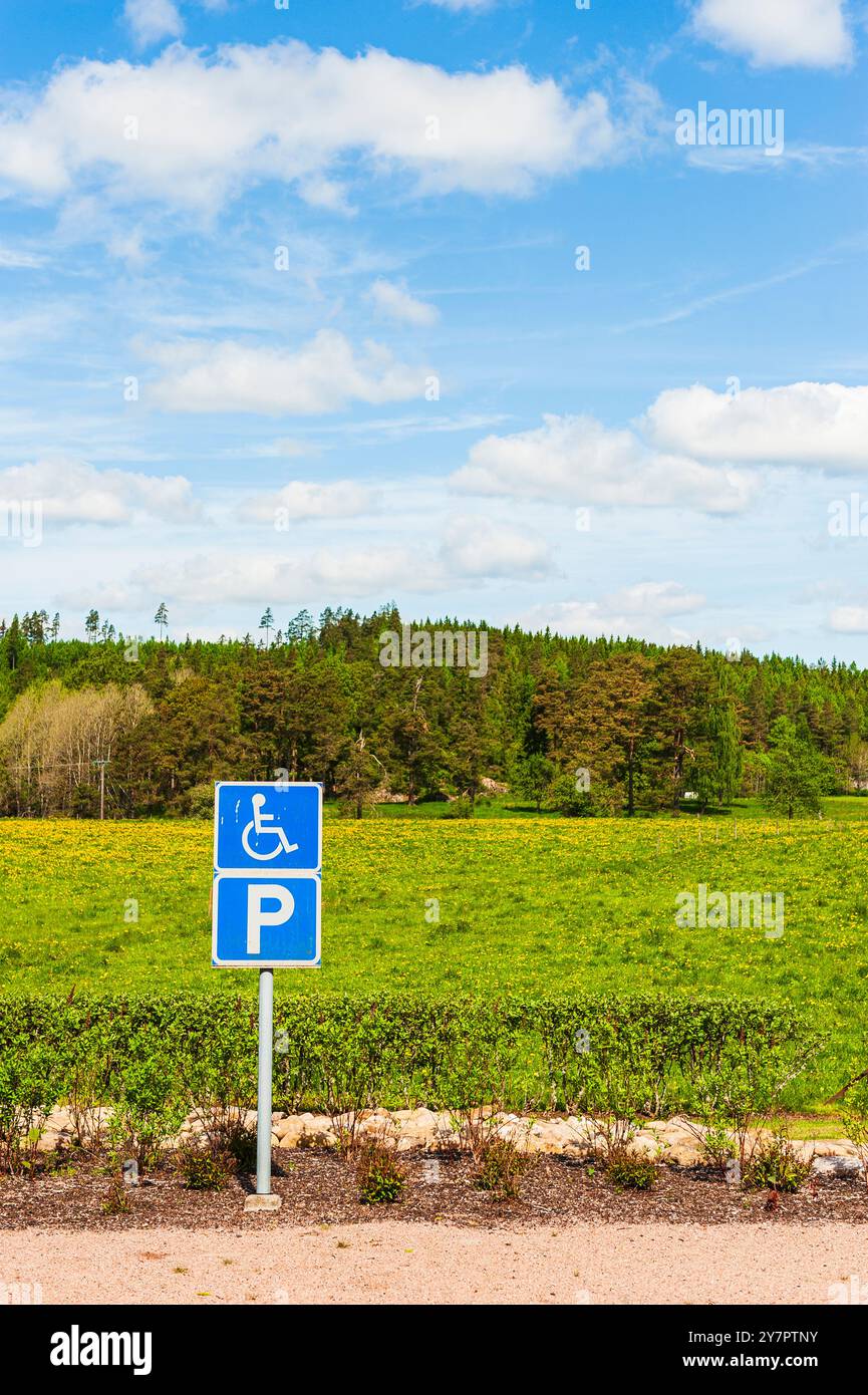 Un panneau de stationnement clair pour handicapés se trouve en évidence dans une région pittoresque de Suède, entourée de champs et d'arbres sous un ciel bleu vif. Le locat Banque D'Images