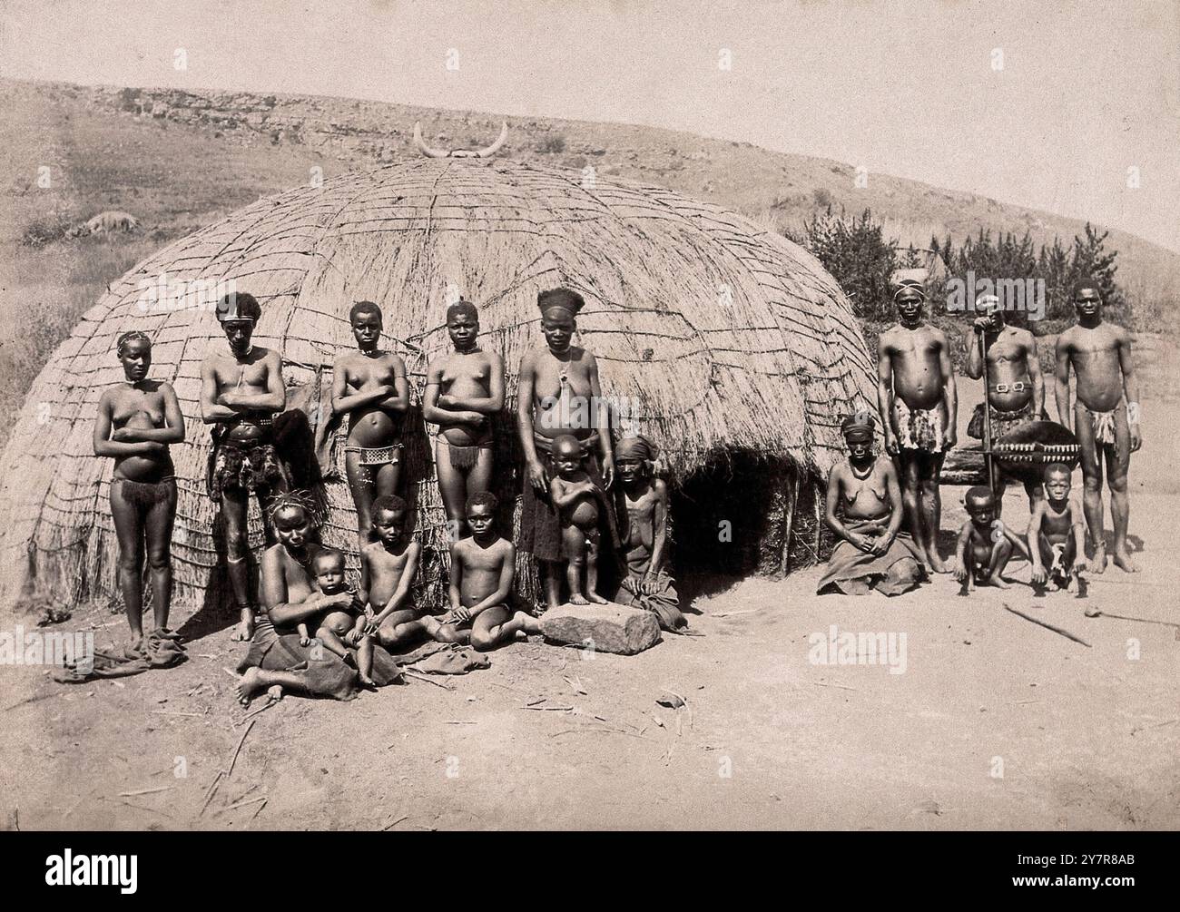 Photographie vintage d'indigènes et de kraal. Africains devant une cabane traditionnelle de kraal. Afrique du Sud, entre 1800 et 1899. Kraal (également orthographié crâne ou kraul) est un mot afrikaans et néerlandais, également utilisé en anglais sud-africain, pour désigner un enclos pour bétail ou autre bétail, situé dans une colonie ou un village d'Afrique australe entouré d'une clôture de branches d'arbustes épines, d'une palissade, d'un mur de boue ou d'une autre clôture, de forme approximativement circulaire. Il est similaire à une boma en Afrique de l'est ou centrale. Banque D'Images