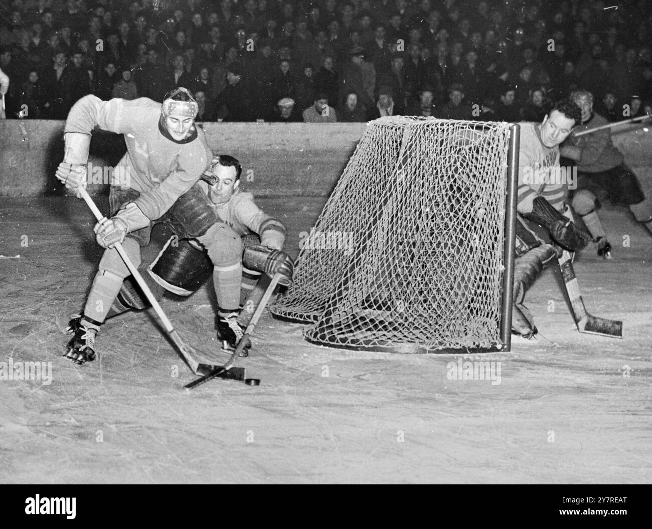 L'ÉQUIPE DE HOCKEY SUR GLACE DE LONDRES remporte LA COUPE AHEARNE L'équipe de hockey sur glace de Londres Harringay Racers a battu l'équipe nationale suédoise, trois couronnes, 7-2 hier pour conserver le trophée Ahearne. Une autre équipe londonienne, les Wembley Lions, a été finaliste de la compétition à trois côtés qui s'est tenue à Stockholm, en Suède. La photo INP montre Pete Belanger, gardien de Harringay, regardant son filet avec anxiété alors que son coéquipier, le défenseur Bill Johnson, tente d'accrocher la rondelle au bâton du Suédois Gosta Johansson. 532/PJ/73717 nouvelles internationales photos. Banque D'Images