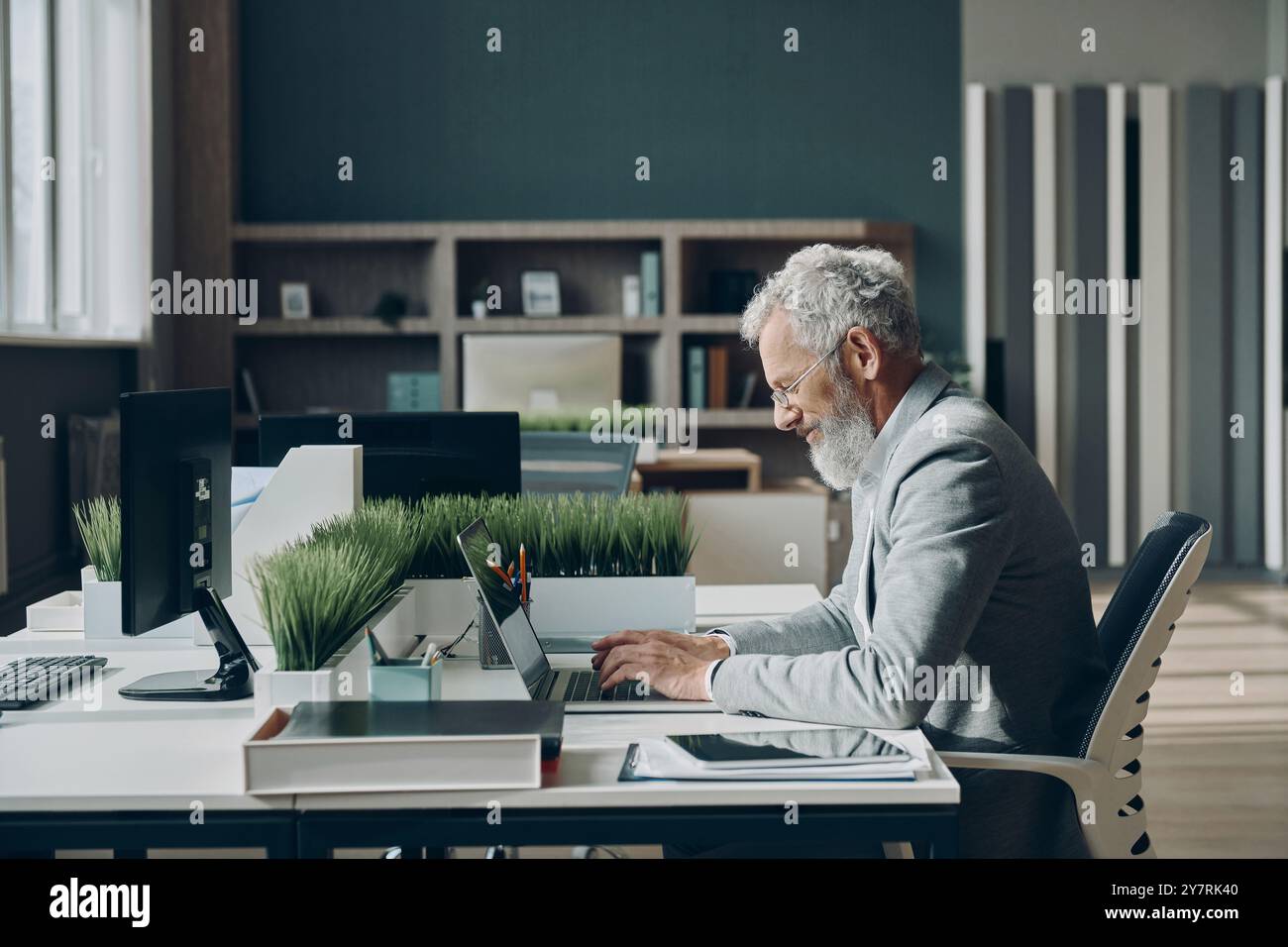 Homme d'affaires mature confiant travaillant sur ordinateur portable tout en étant assis à son lieu de travail dans le bureau Banque D'Images