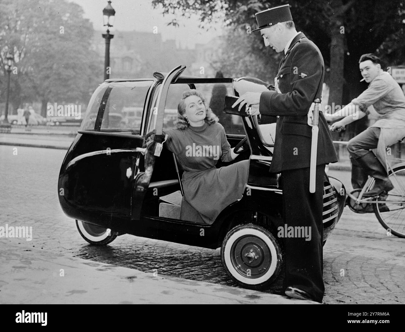 SCOOTER DE VOITURE DE FRANCE. Le 16.10.53, un nouveau véhicule sera bientôt vu en train de se frayer un chemin dans le tristement célèbre trafic de la capitale française lorsqu'un scooter de conception italienne et de construction française y sera mis sur le marché. Le 'Microbo' est un trois roues, deux places avec un moteur de scooter de 125 cm3 monté dans une carrosserie en plexiglas, recouverte de toile. Il est capable de 45 mph. INP photo montre le policier français qui a vu le Microbo testé à Paris n'a pas pu résister à l'arrêter quand il a vu la star de cinéma Huguette Montréal au volant. Photos d'actualités internationales. Banque D'Images