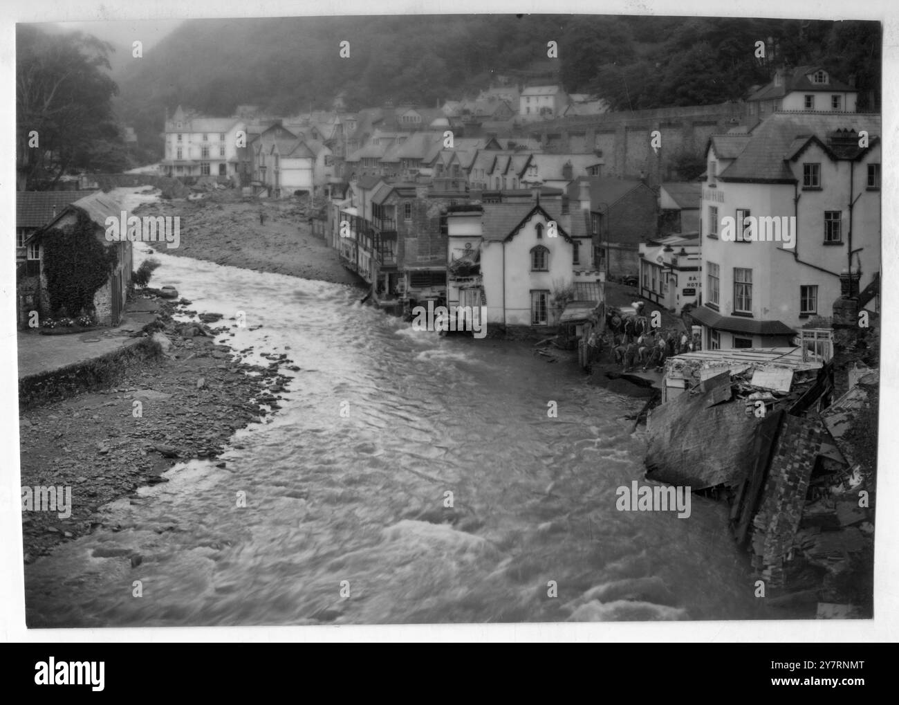 NETTOYAGE DES DÉGÂTS CAUSÉS PAR LES INONDATIONS DANS LA BOUCHE DE LYNMOUTH FRAPPÉE. Lynmouth, North Devonshire : alors que les eaux de crue diminuent lentement dans Lynmouth frappée, les ouvriers commencent à travailler sur le défrichement de la High Street (à droite). La route se termine maintenant dans un torrent furieux , le pont a été balayé. Les dommages à Lynmouth sont sans précédent dans l'histoire du comté de West. 18 août 1952 Banque D'Images