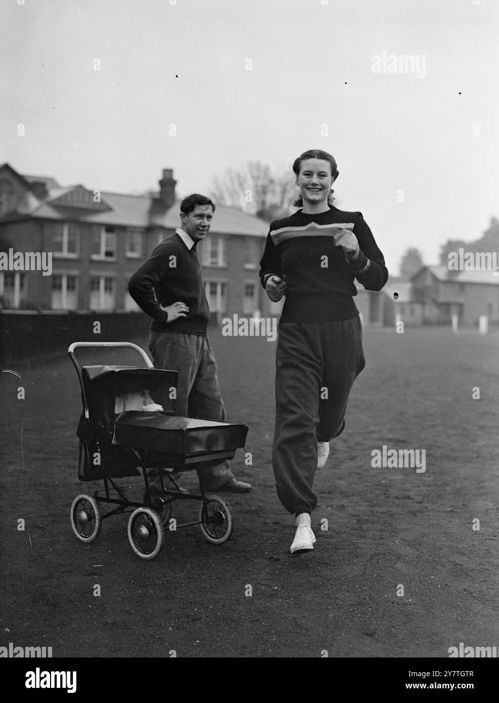 L'ENTRAÎNEMENT DE MAUREEN EST UNE AFFAIRE DE FAMILLE MAINTENANT 5 novembre 1949 pour la première fois depuis la naissance de son bébé, Maureen Gardner, un record britannique de haies olympiques, s'entraînait au London University Ground à Motspur Park, Surrey. Maureen qui a l'œil sur une éventuelle rencontre avec sa rivale olympique, Fanny Blankers Koen aux Championnats d'Europe à Bruxelles en août prochain s'entraîne sous la supervision de son mari Geoffery Dyson, entraîneur national britannique. Image montre : seulement la moitié de sa famille, son mari Geoff Dyson, regarde Maureen Gardner à l'entraînement. L'autre moitié Timothée, dort Banque D'Images