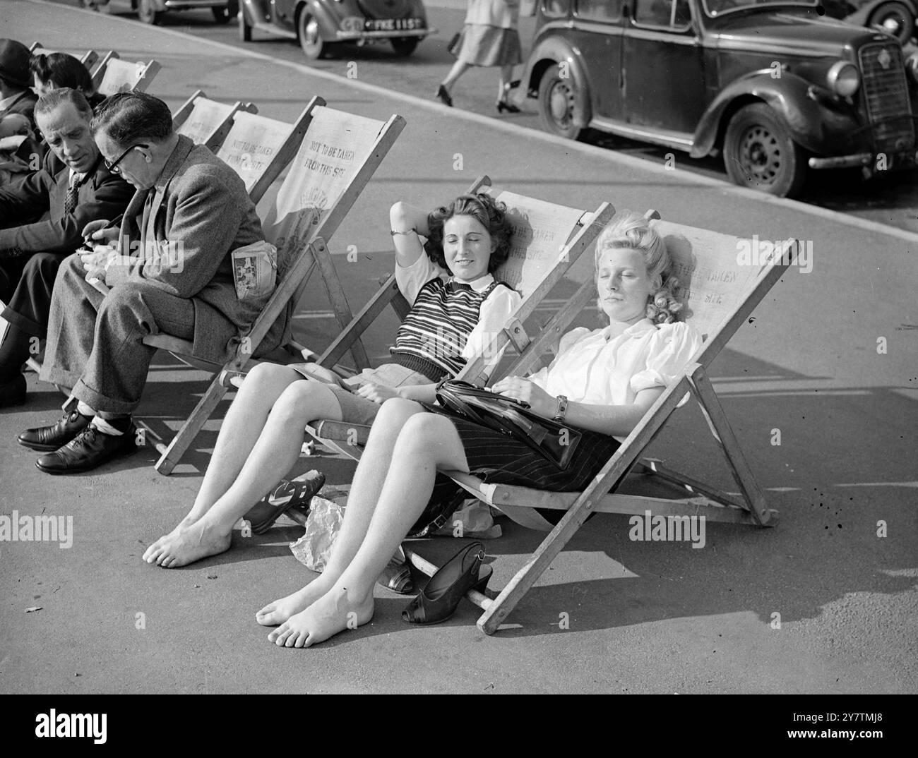 Chaussures off à Brighton - journée la plus chaude de l'année à BrightonBrighton a enregistré la journée la plus chaude de l'année avec une température de 80 degrés . De grandes foules affluaient vers la côte et les plages de Brighton étaient remplies par des vacanciers tardifs profitant de la vague de chaleur inattendue de l'automne. Photos : deux visiteurs londoniens Shirley O'Sullivan (à gauche) et Vicki Forrest (à droite) enlèvent leurs chaussures et font une sieste sous le soleil brillant sur la promenade de Brighton , West Sussex 29 septembre 1946 Banque D'Images