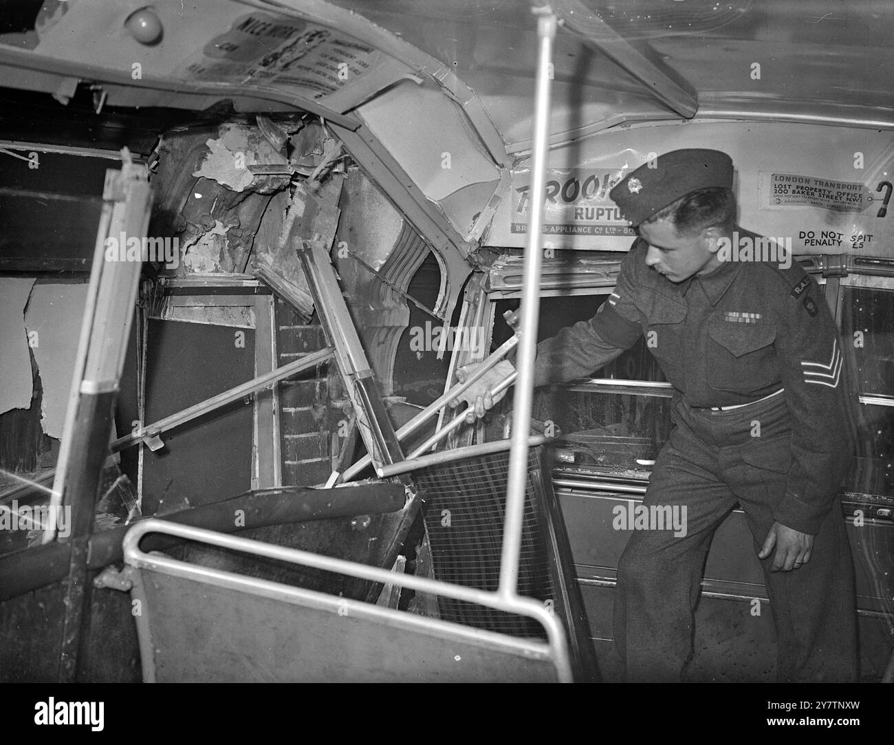 LA TEMPÊTE LONDONIENNE DÉRACINE LES BARRAGES ROUTIERS - PROVOQUE L'ÉCRASEMENT D'UN BUS DANS UN MAGASIN - 13 PERSONNES BLESSÉES. La terrible tempête qui a éclaté sur Londres a provoqué le déracinement des barrages routiers dans Kensington High Street. Un bus de 49 a dérapé sur les barrages routiers déracinés et s'est écrasé dans une vitrine. 13 personnes ont été blessées et transportées à l'hôpital avec 3 sérieusement. Photo montre : le sergent J C Meldrum RASC d'Ilford qui a appelé une ambulance de l'armée et a aidé à faire sortir les blessés du bus, vu examiner la damamge sur le pont supérieur de l'autobus écrasé. 26 juillet 1946 Banque D'Images