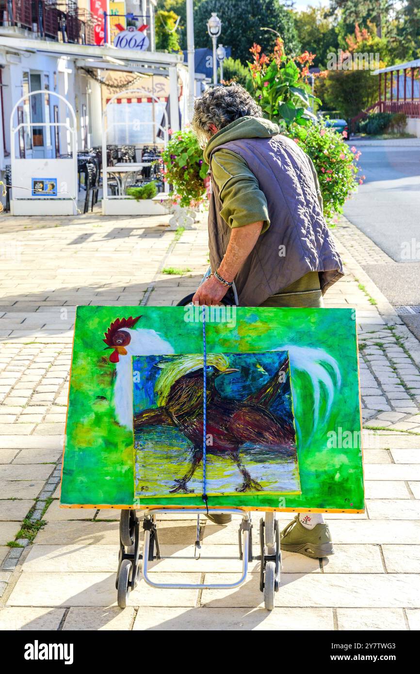 Femme artiste amateur tirant chariot avec des œuvres d'art en toile le long du trottoir - la Roche Posay, Vienne (86), France. Banque D'Images