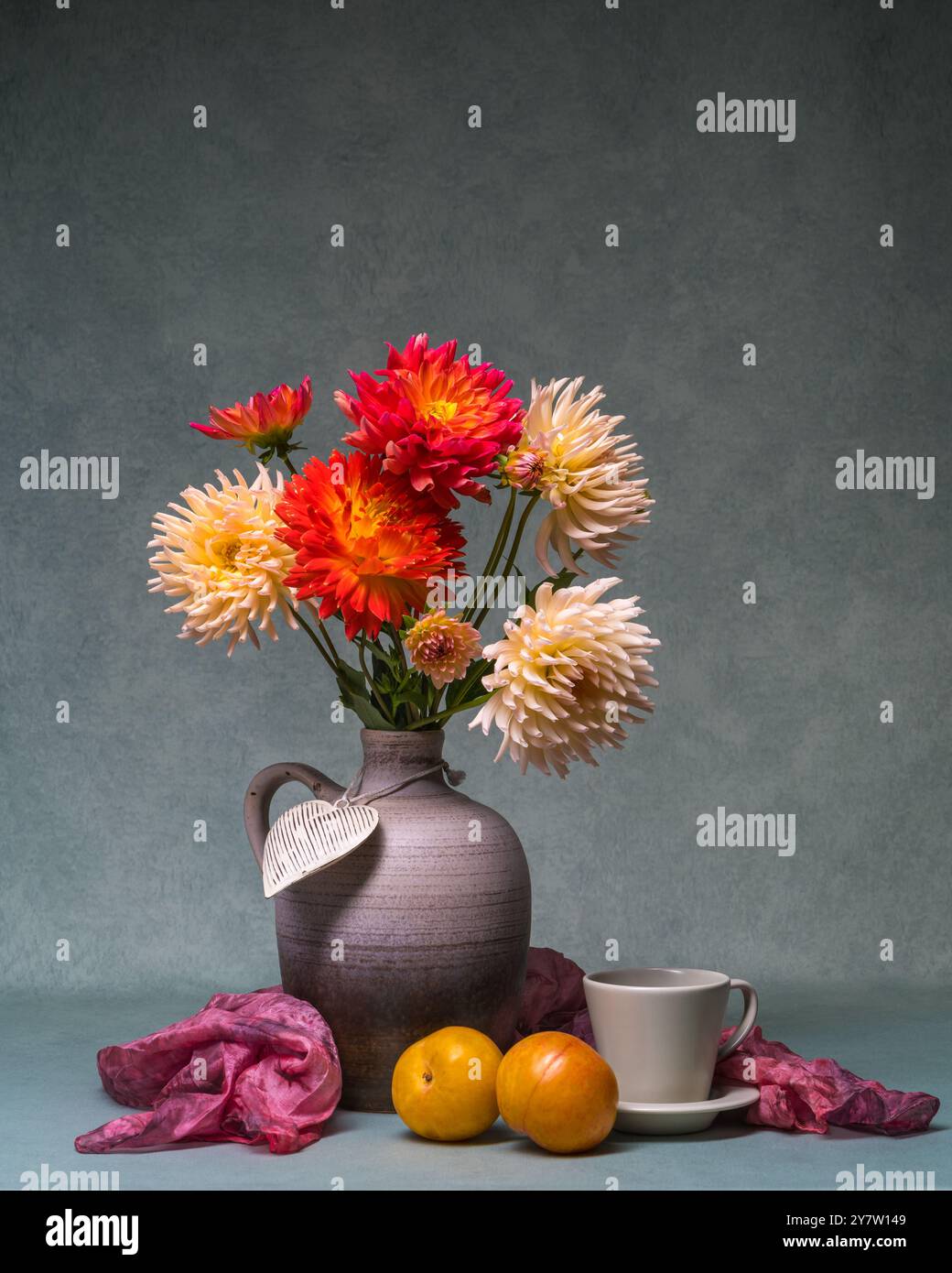 Fleurs d'automne lumineuses. Bouquet luxuriant de dahlias de différentes couleurs dans un grand vase. A côté de se coucher deux prunes jaunes, tasse. La nature morte crée une atmosphère de Banque D'Images