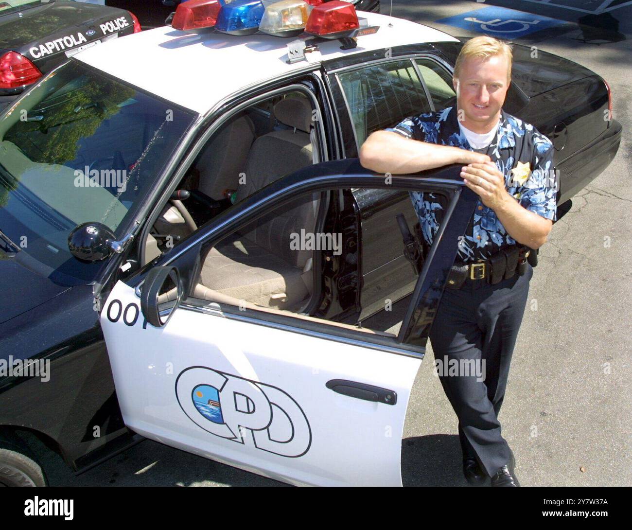 Capitola, Californie : L'officier Andrew Dally, avec le département de police de Capitola, se tient à côté de sa voiture de patrouille le lundi 6 août 2001 portant leur uniforme d'été optionnel, une chemise hawaïenne avec numéro d'insigne. L'idée est de rendre la police plus accessible. De nombreux résidents de Capitola se rendent à leur travail dans la Silicon Valley. Banque D'Images