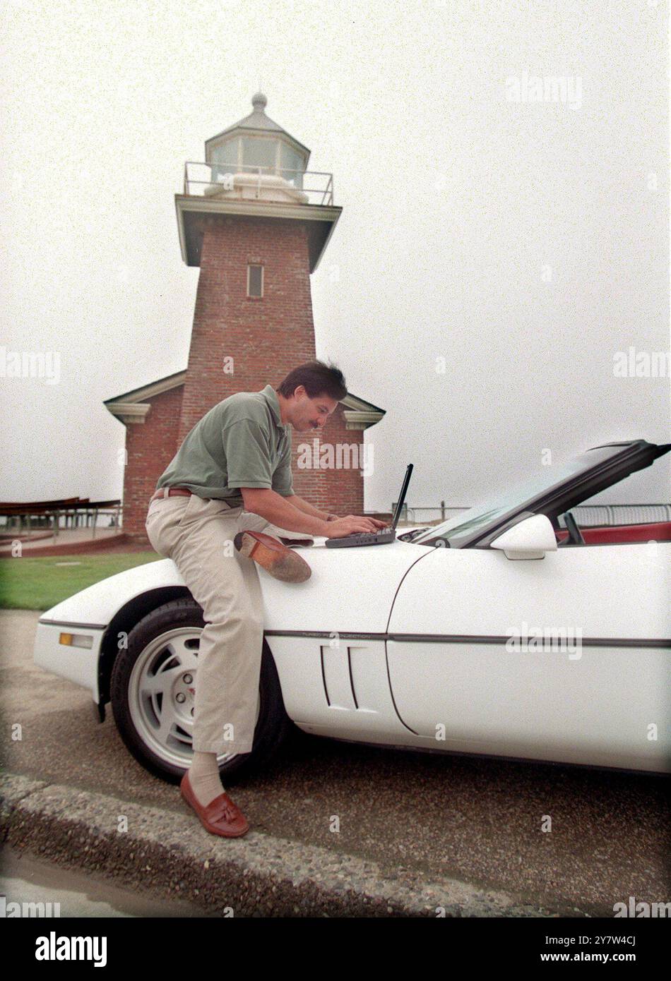 Santa Cruz, Californie : Rick Armillotto est administrateur système chez Thuridion, une société de logiciels de Santa Curz. Ici, il travaille sur un ordinateur portable sur le capot de sa Corvette 1990 près du phare de Santa Cruz. Le phare abrite un musée du surf. Banque D'Images