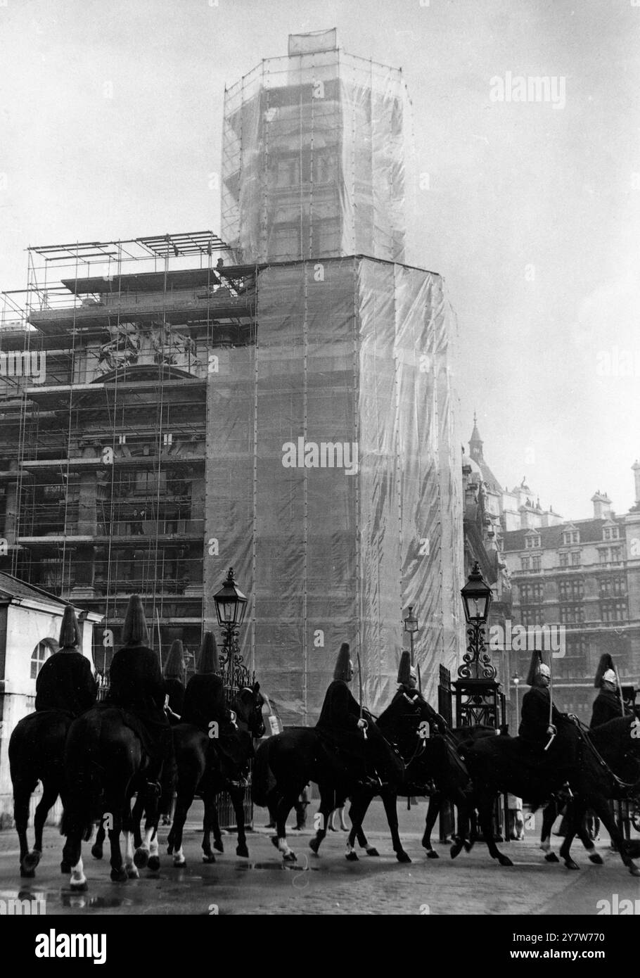 Alors que les célèbres « Horseguard » de Londres arrivent à Whitehall aujourd'hui, pour la cérémonie de la relève de la garde, le bâtiment du War Office (en arrière-plan) subit une expérience de nettoyage. Le bâtiment abrité dans un « cocon » en polyéthylène est nettoyé et peint par London Stone, qui a nettoyé la colonne Nelson. Ils expérimentent dans le nettoyage de la façade des bâtiments publics dans tous les types de conditions météorologiques, pour prouver que des travaux d'entretien extérieur peuvent être effectués sur les bâtiments pendant les mois d'hiver, Londres, Angleterre.29 janvier 1969 Banque D'Images