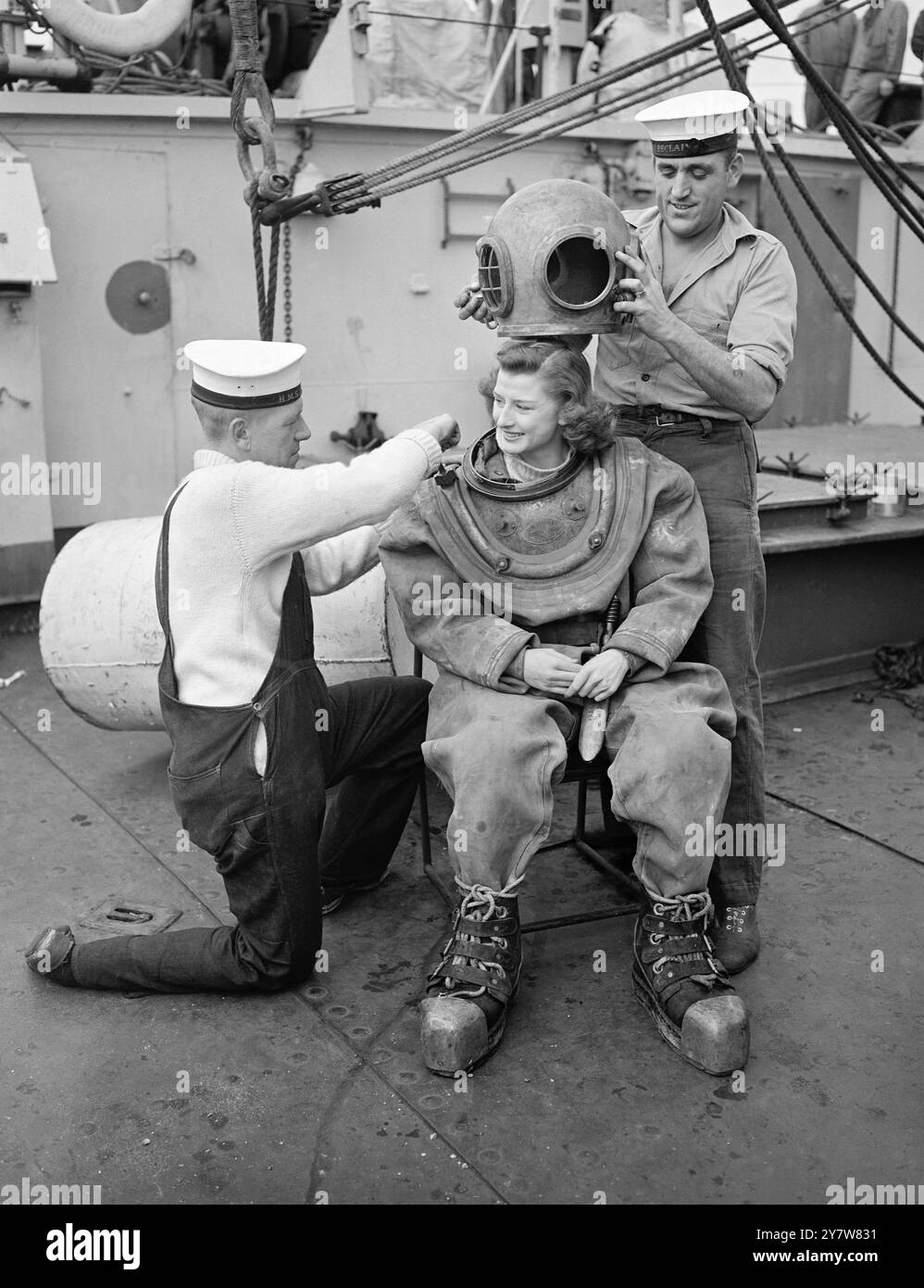 Anita D'Ray, 21 ans, film 'Starlet' est aidé dans une combinaison de plongée standard par les marins Frank Frost (à gauche) et Bert Bull (à droite) à bord du navire expérimental de plongée profonde de la Royal Navy HMS Recclaim à Chatham. Miss D'Ray est la mascotte du navire et lors d'une visite au navire, elle a été persuadée par les officiers et les hommes d'essayer un équipement de plongée. Née à Molesey Surrey, Miss D'Ray a commencé sa carrière sur scène avec la Croix-Rouge américaine à l'âge de 14 ans. Elle a rejoint le Windmill Theatre en 1944 et l'année dernière a commencé à apparaître dans des films. Mis à part sa carrière d'actrice, Miss D'Ray s'intéresse en premier lieu au vol Banque D'Images