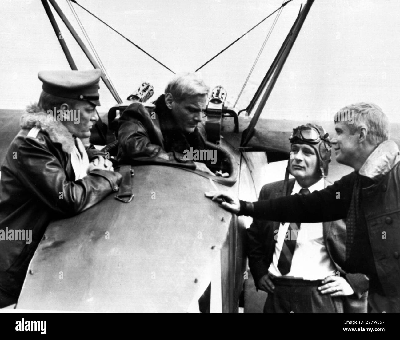 Dublin : L'acteur Carl Schell assis dans le cockpit d'un triplan Fokker de la première Guerre mondiale discutant avec l'homme qui joue dans le film ' The Blue Max ' , baron von Richthofen ( deuxième à partir de la droite ) qui était un as aérien allemand de la première Guerre mondiale . La star du film George Peppard ( à droite ) et Jeremy Kemp ( à gauche ) écoutent la conversation 17 août 1965 Banque D'Images