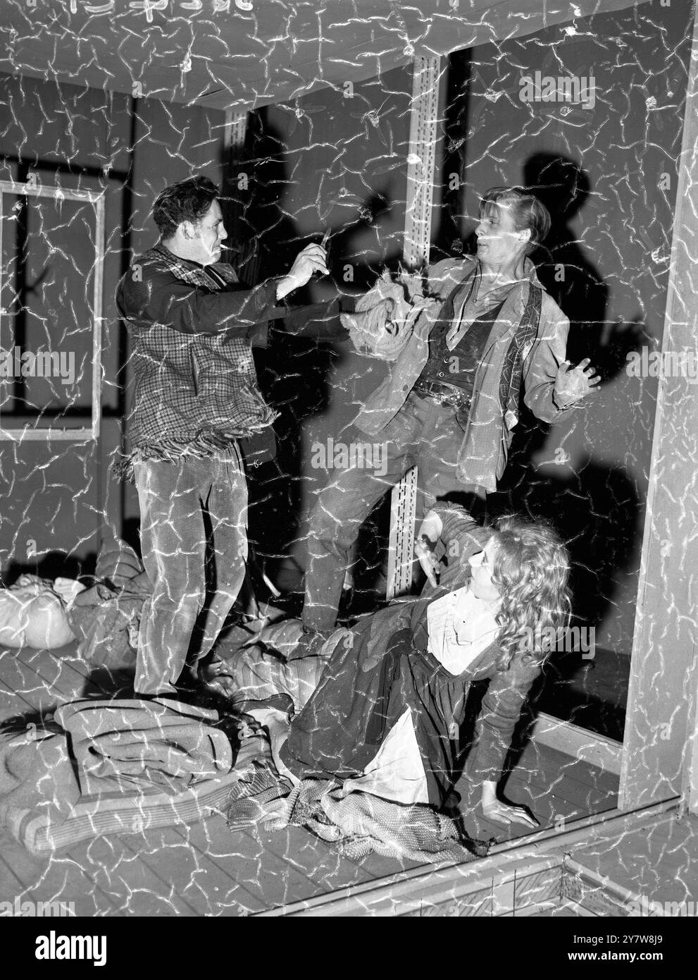 ' Vivez comme des cochons ' vient à la Royal CourtLondres : vivre comme des cochons - et se battre comme des animaux - Robert Shaw (tenant un couteau ) , Alan Dobie et Frances Cuka se querellent dans une maison sur un domaine d'après-guerre dans une ville industrielle du Nord du pays . La scène dramatique n'est cependant qu'une répétition de la représentation d'ouverture de ' Live Like Pigs ' , qui sera donnée par la English Stage Company au Royal court Theatre . Dobie joue ' Col ' , ' Shaw joue ' Blackmouth ' , et Miss Cuka joue ' Daffodil ' , le jeu rugueux et prêt . Auteur de la pièce , John Arden , une dramaturgie du Yorkshire de 28 ans Banque D'Images