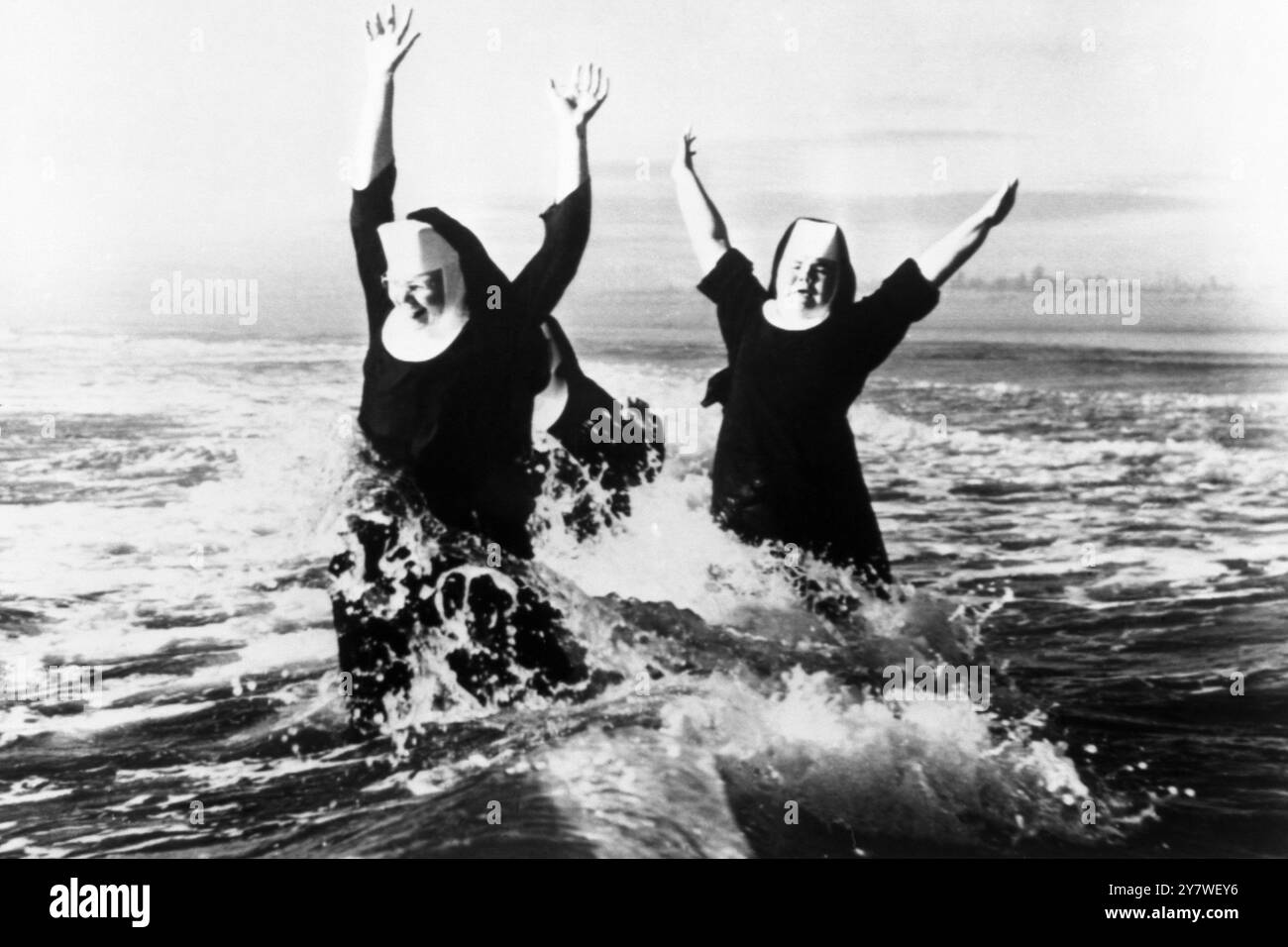 Les armes sont jetées haut dans le plaisir par les sœurs Ruth (à gauche) et Agnes comme des cascades de surf autour d'eux sur une plage à Grayland , Grays Harbour County , Washington . En partie cachée à l'arrière est sœur Rita. Elles sont trois des sept sœurs de l’ordre de Saint-Benoît qui ont passé une semaine sur le bord de la mer dans le cadre d’un nouveau programme de vacances. 23 août 1960 Banque D'Images