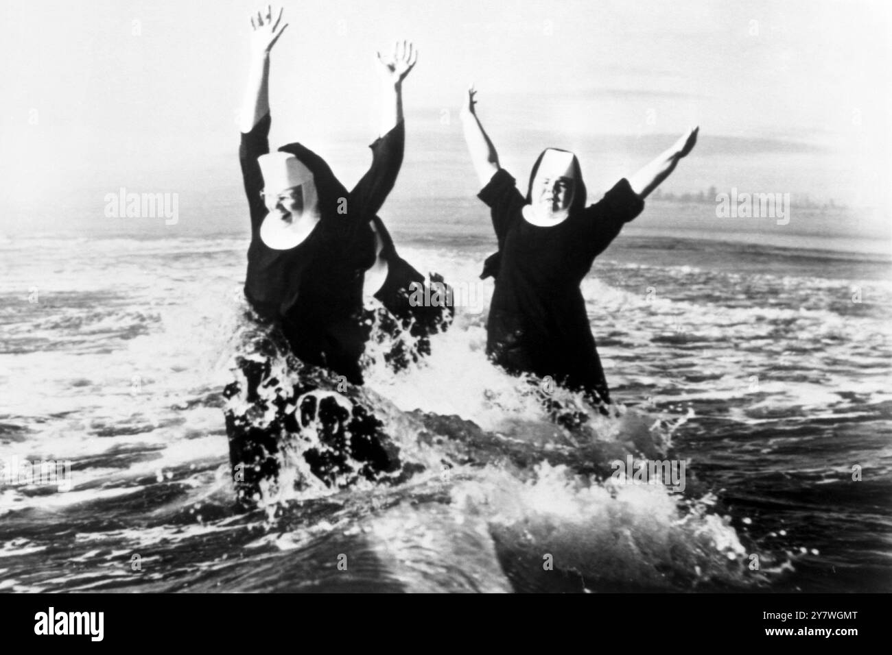 Les armes sont jetées haut dans le plaisir par les sœurs Ruth (à gauche) et Agnes comme des cascades de surf autour d'eux sur une plage à Grayland , Grays Harbour County , Washington . En partie cachée à l'arrière est sœur Rita. Elles sont trois des sept sœurs de l’ordre de Saint-Benoît qui ont passé une semaine sur le bord de la mer dans le cadre d’un nouveau programme de vacances. 23 août 1960 Banque D'Images