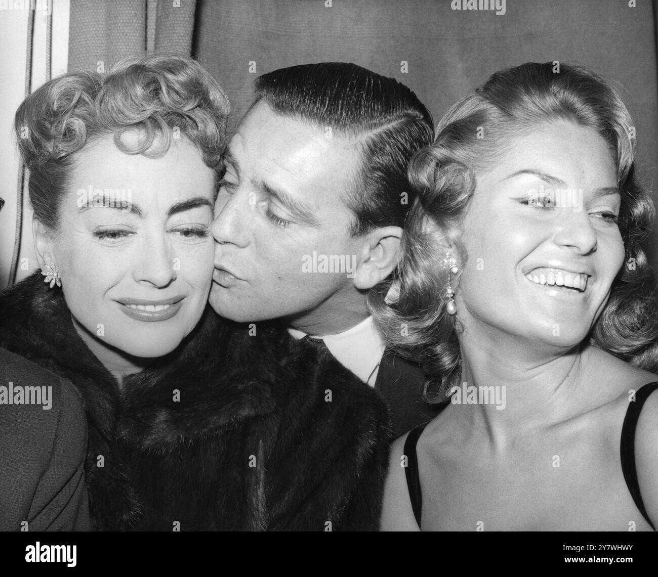 Le comédien Norman Wisdom donne un baiser à l'actrice Joan Crawford pour lui souhaiter bonne chance quand elle sera présentée à la reine à la représentation de film royal de la bataille de la rivière plate à l'Odéon , Leicester Square , Londres. Profitant de la blague ici est Belinda Lee qui est également à présenter. Ils assistaient à une réception donnée à l'Odéon , Marble Arch pour les stars qui doivent être à l'exposition royale. 26 octobre 1956 Banque D'Images