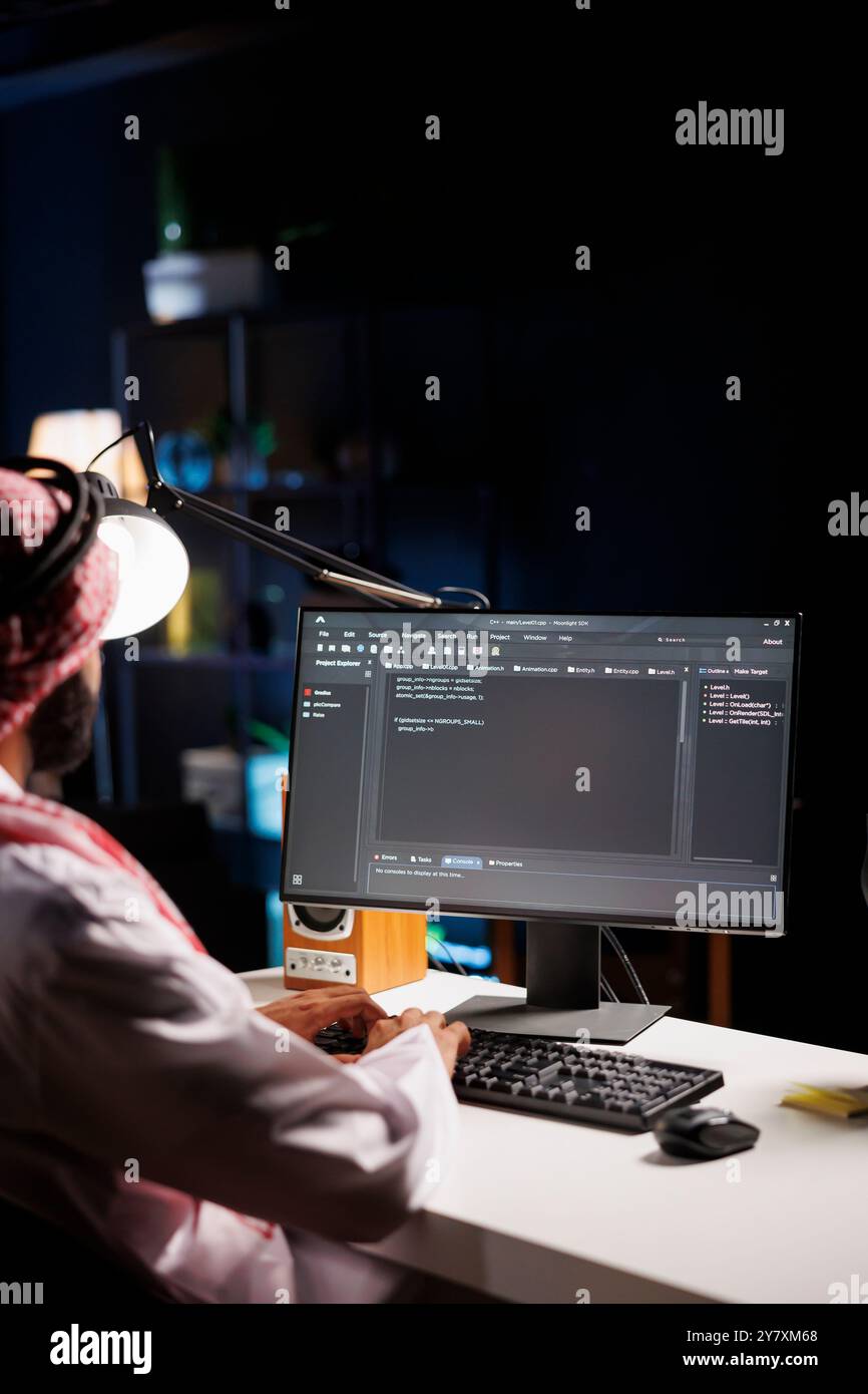 Un développeur traditionnel du moyen-Orient compile du code sur un ordinateur de bureau, mettant en valeur son expertise en programmation, algorithmes et développement de logiciels. Focalisation sélective sur le moniteur pc affichant le code source. Banque D'Images