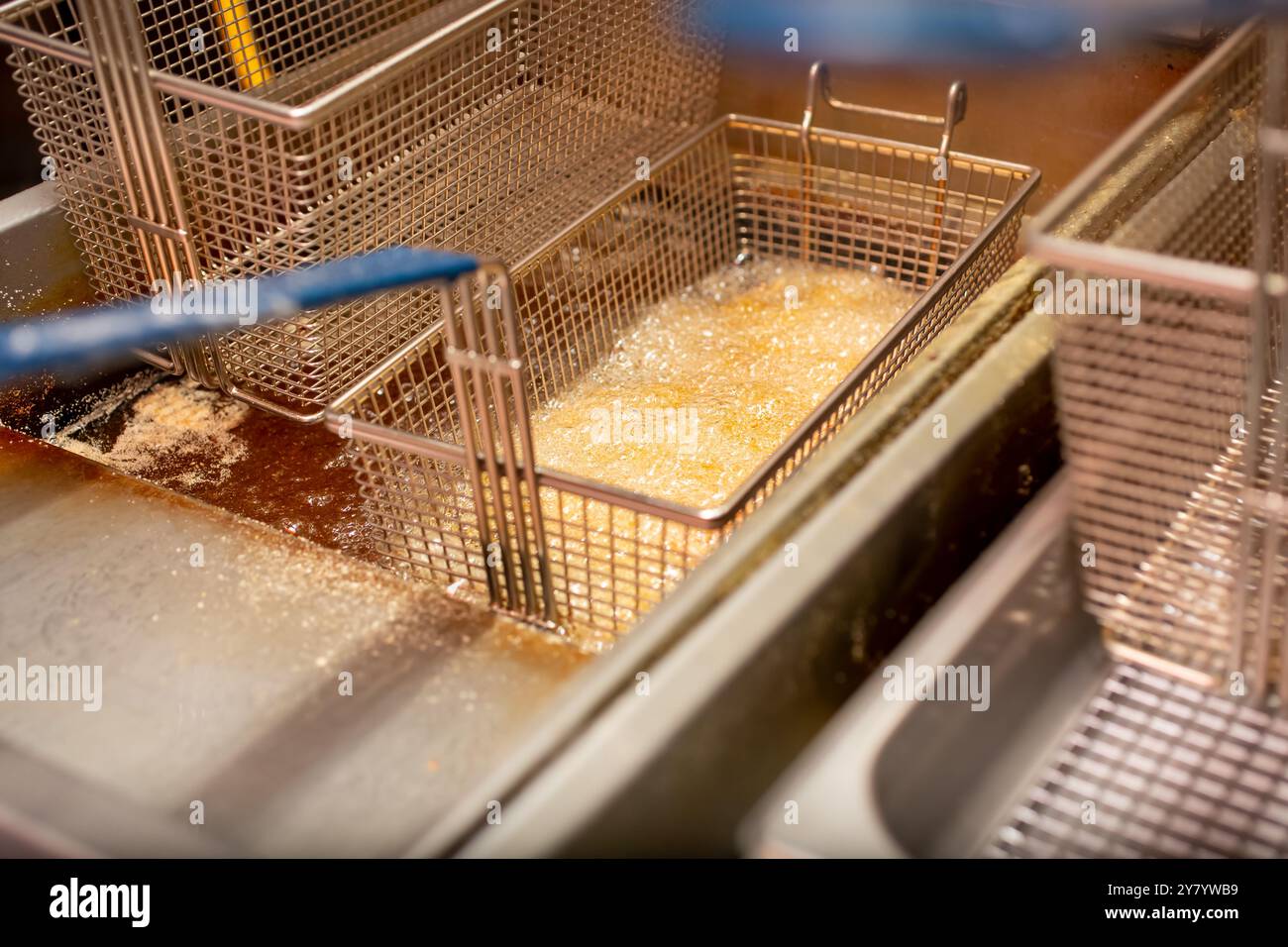 Une vue d'un panier de contenu alimentaire friture et bouillonnement dans la graisse chaude et l'huile, dans un cadre de cuisine de restaurant. Banque D'Images