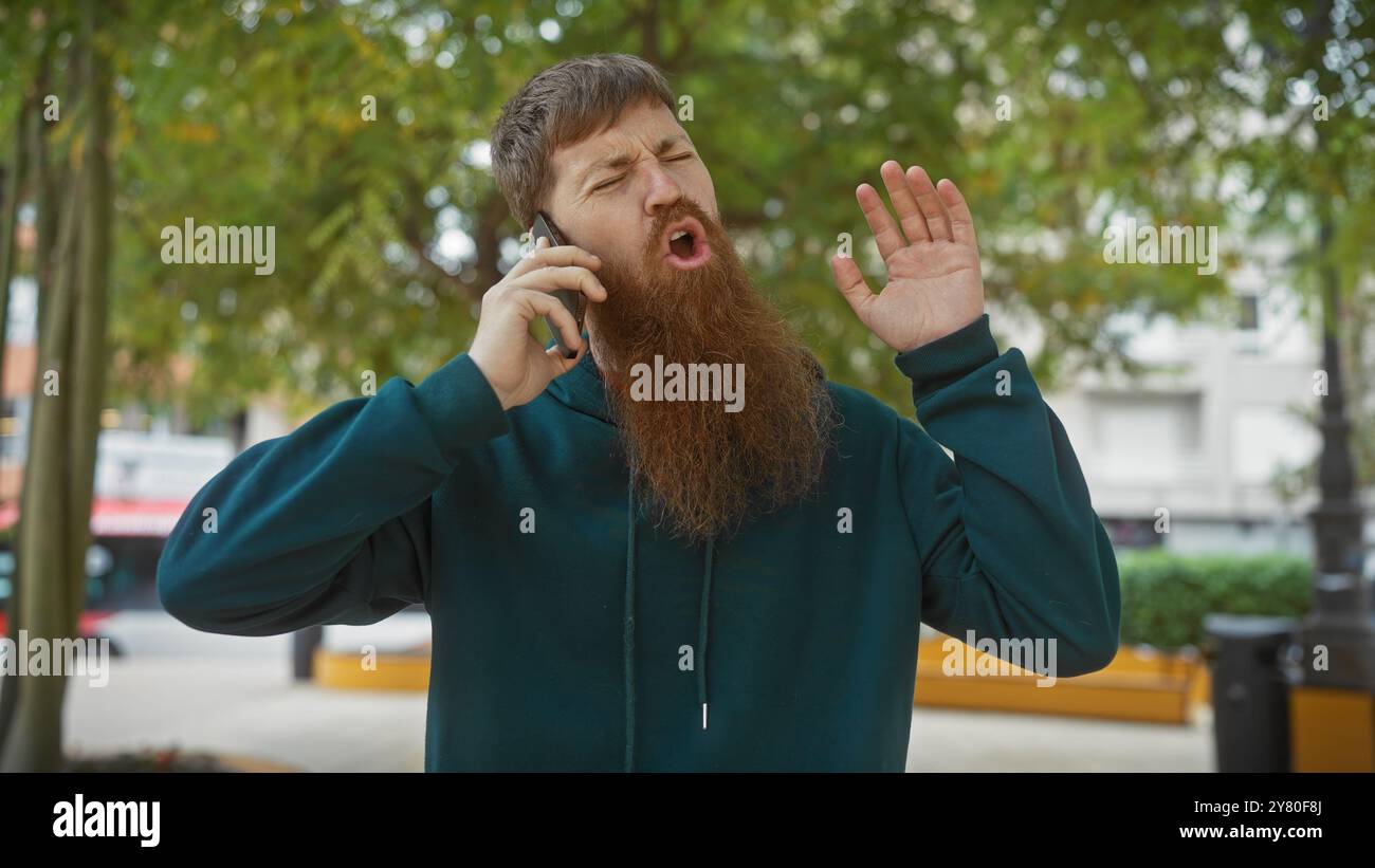 Homme barbu en détresse sur un appel dans le parc de la ville Banque D'Images