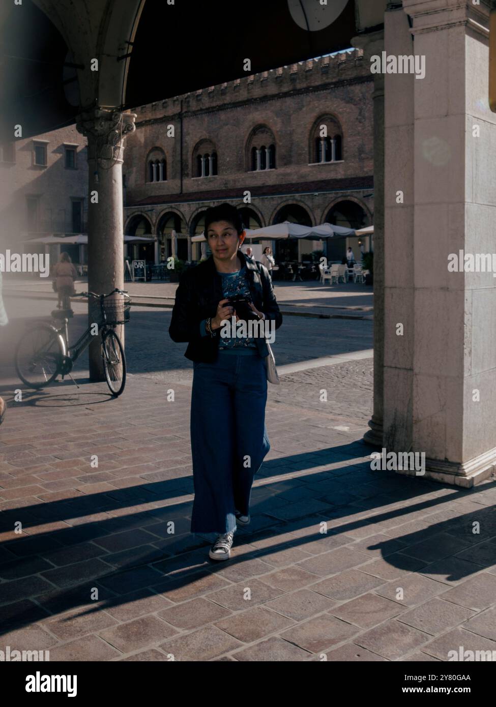 Mantoue, Italie 30 septembre 2024 Une touriste consulte son smartphone sur une place du centre historique de mantoue, italie, avec un restaurant dans la BA Banque D'Images