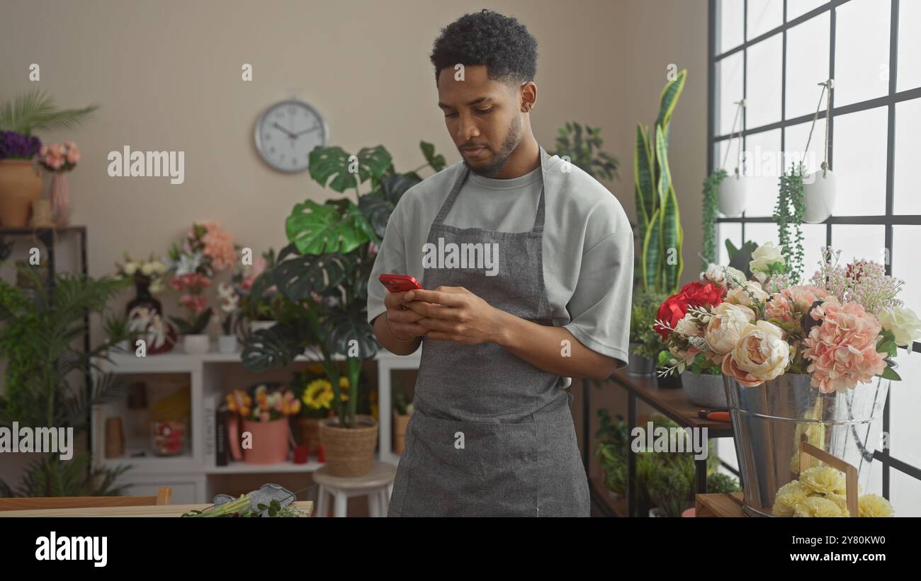 Un homme afro-américain dans un magasin de fleurs regardant son téléphone entouré de plantes et de bouquets. Banque D'Images