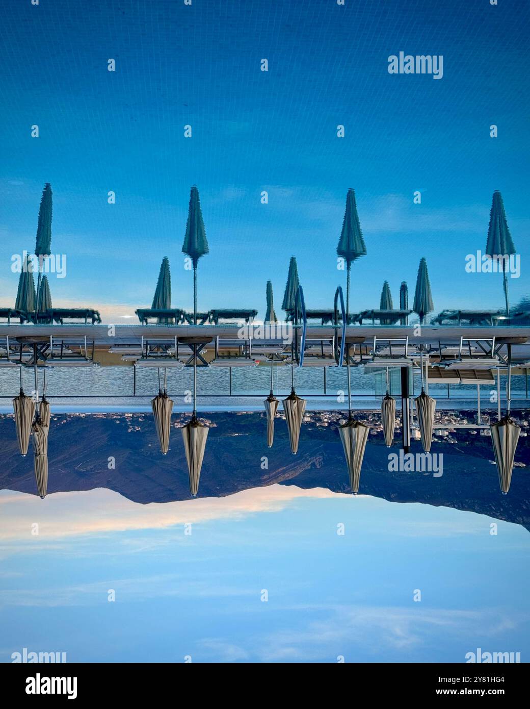 Photo inversée de piscine avec parasols, ciel et montagnes reflétés. Banque D'Images