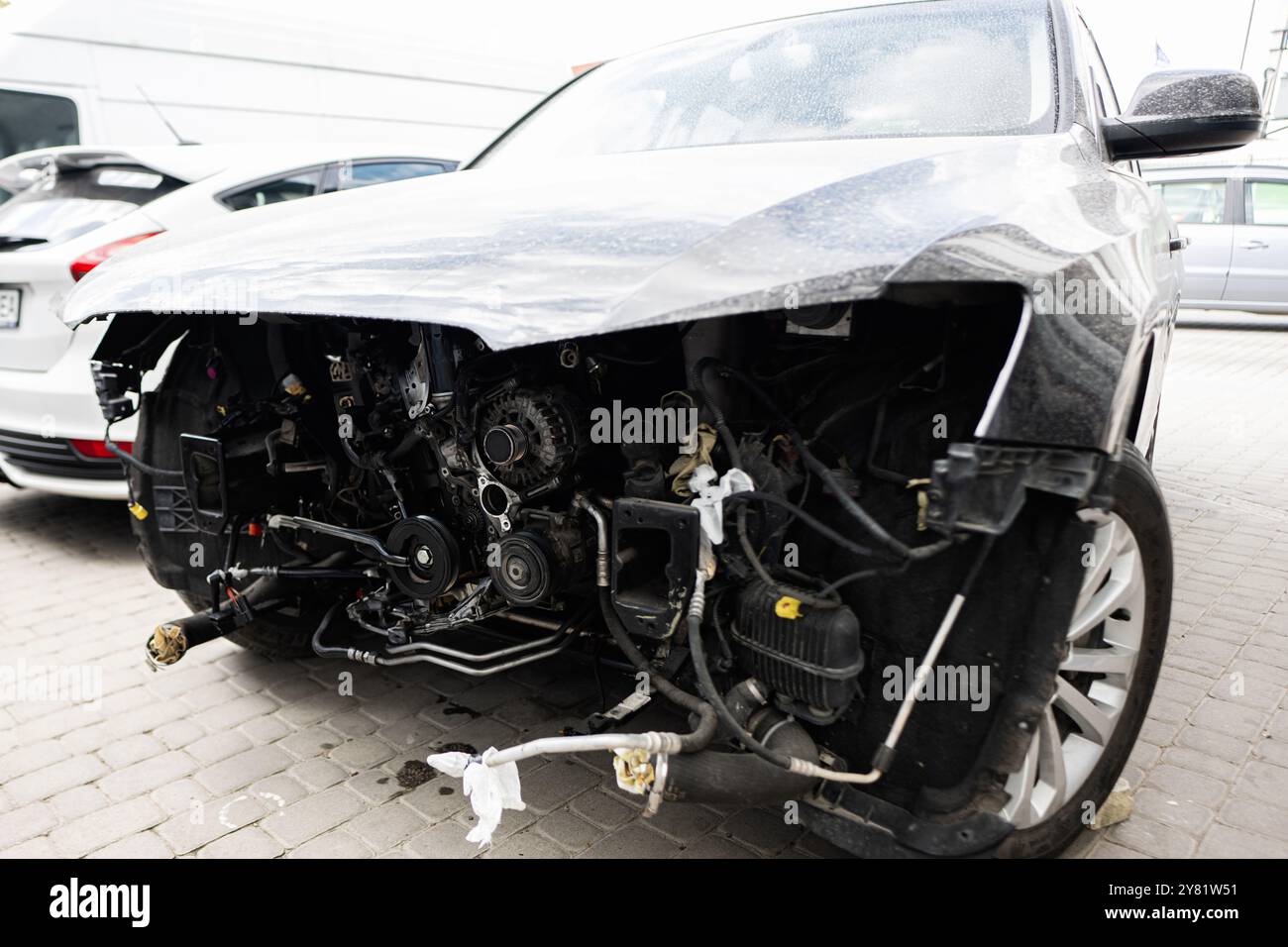 Gros plan d'une voiture avec un pare-chocs avant endommagé et des pièces de moteur exposées. Le véhicule est garé dans un parking extérieur, mettant en évidence les conséquences d'un acci Banque D'Images