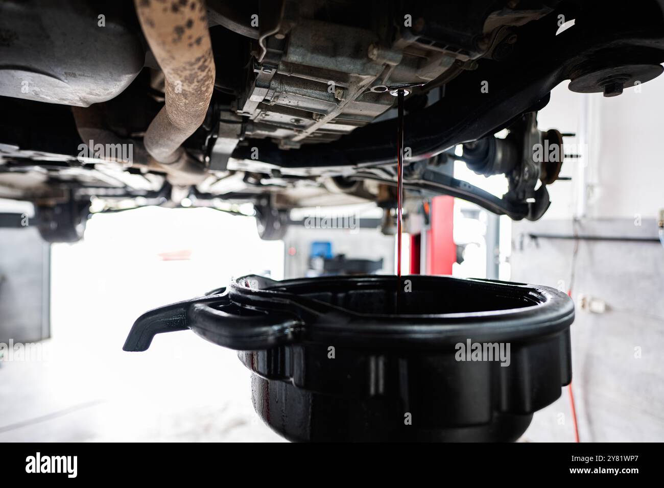 Une vue détaillée d'une vidange d'huile ayant lieu dans un garage de réparation automobile. L'huile s'écoule du moteur de la voiture dans un bac de récupération. Banque D'Images