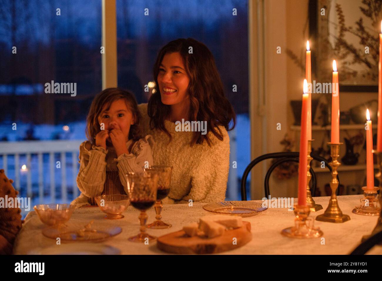 Une femme souriante et un jeune enfant apprécient un dîner aux chandelles confortable à l'intérieur. Banque D'Images