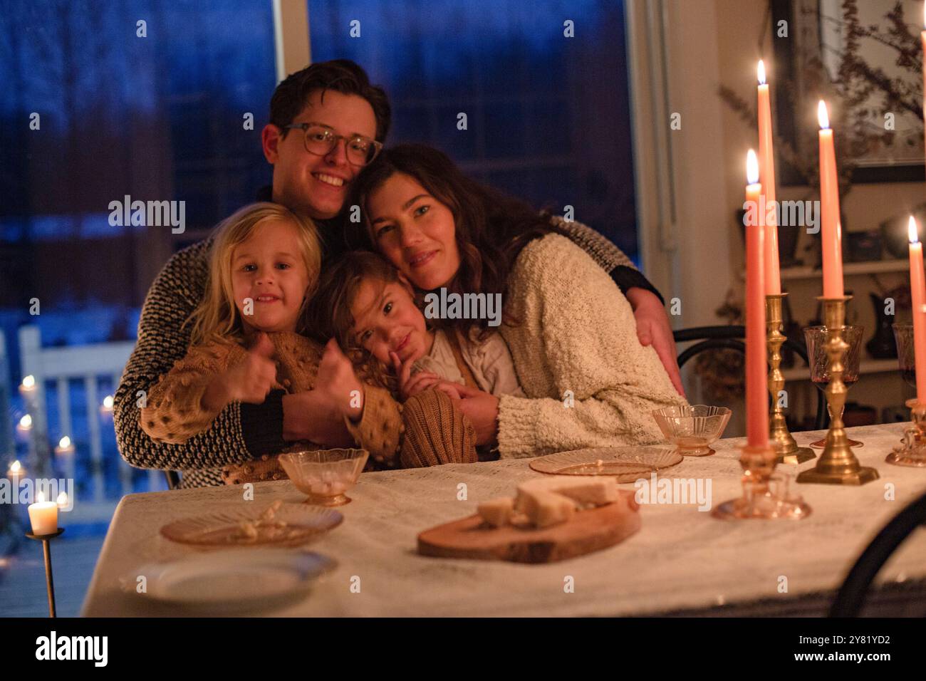 Une famille profite d'un dîner confortable aux chandelles, souriant et s'embrassant à une table décorée de façon festive. Banque D'Images