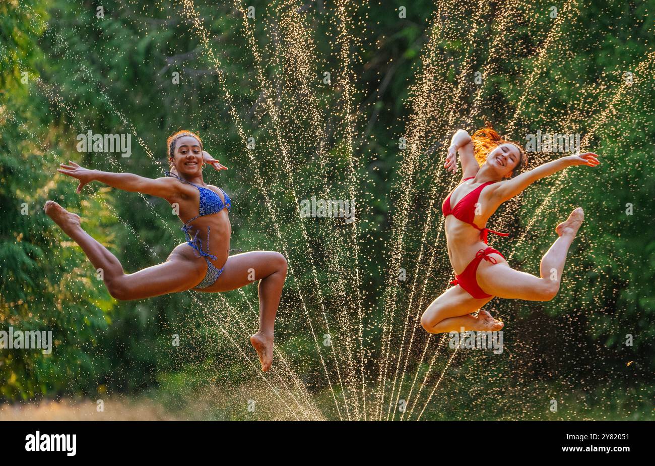 Deux femmes joyeuses bondissant à travers les arrosages par une journée ensoleillée Banque D'Images