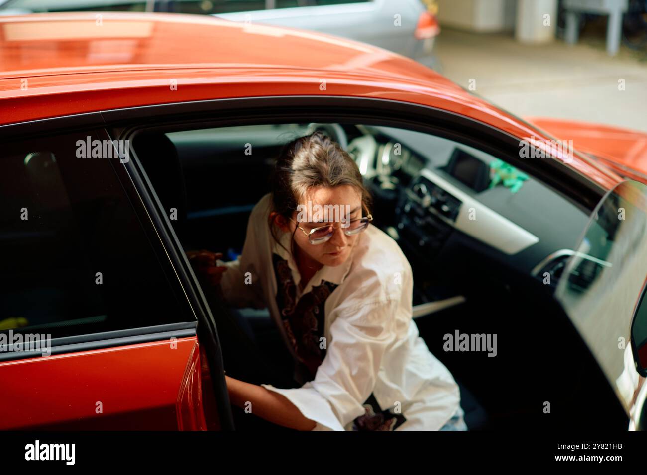 Une femme en chemise blanche monte dans une voiture rouge avec la porte ouverte. Banque D'Images