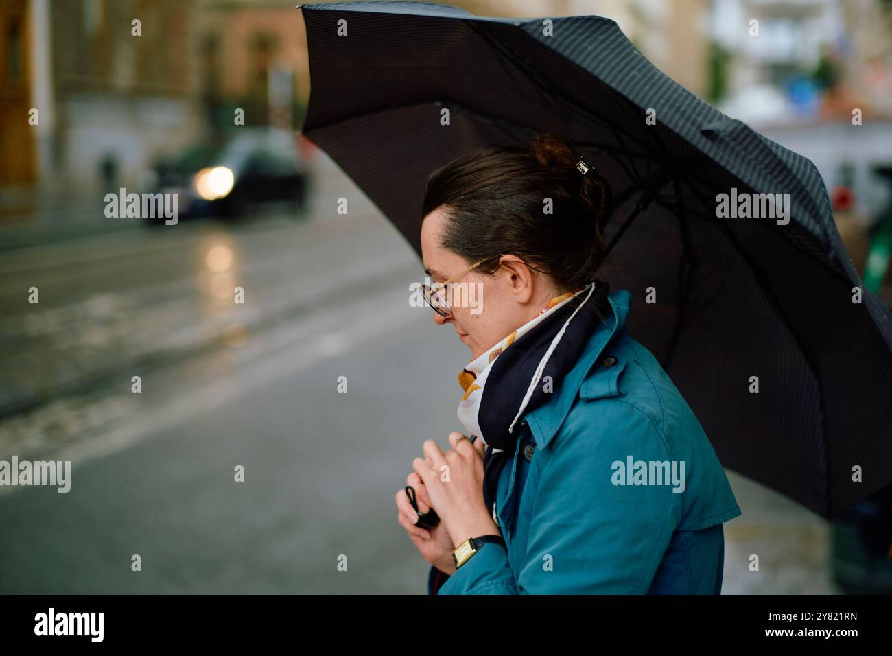 Profil latéral d'un adulte avec un parapluie noir sur une rue pluvieuse de la ville. Banque D'Images