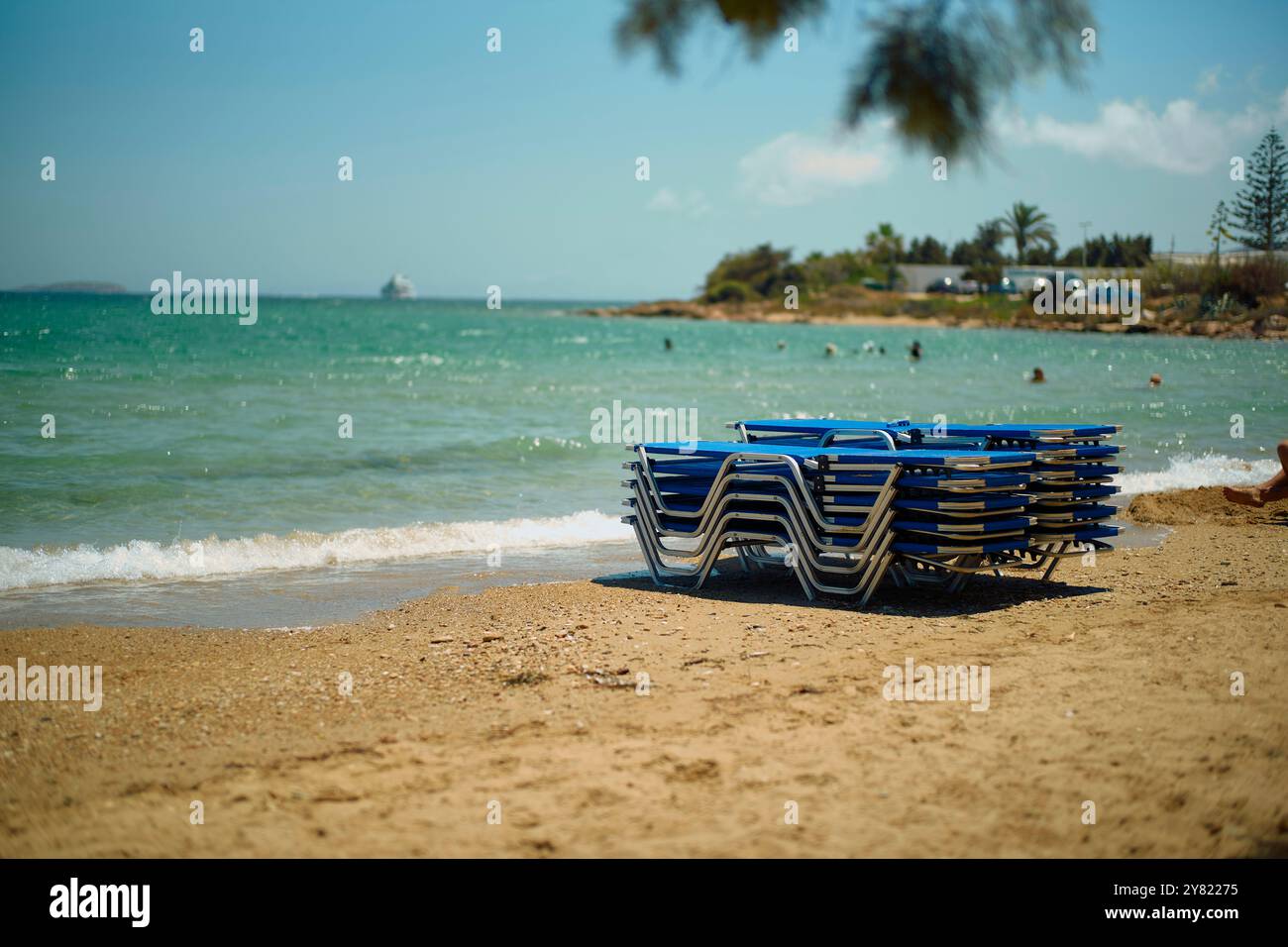 Chaises de plage bleues empilées sur un rivage de sable avec des vagues s'écrasant doucement et un ciel bleu clair au-dessus de vous. Banque D'Images