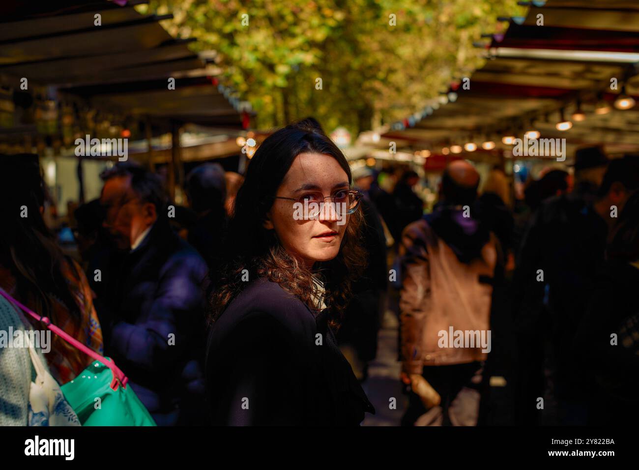 Femme avec des lunettes regardant par-dessus son épaule dans un marché extérieur bondé. Banque D'Images