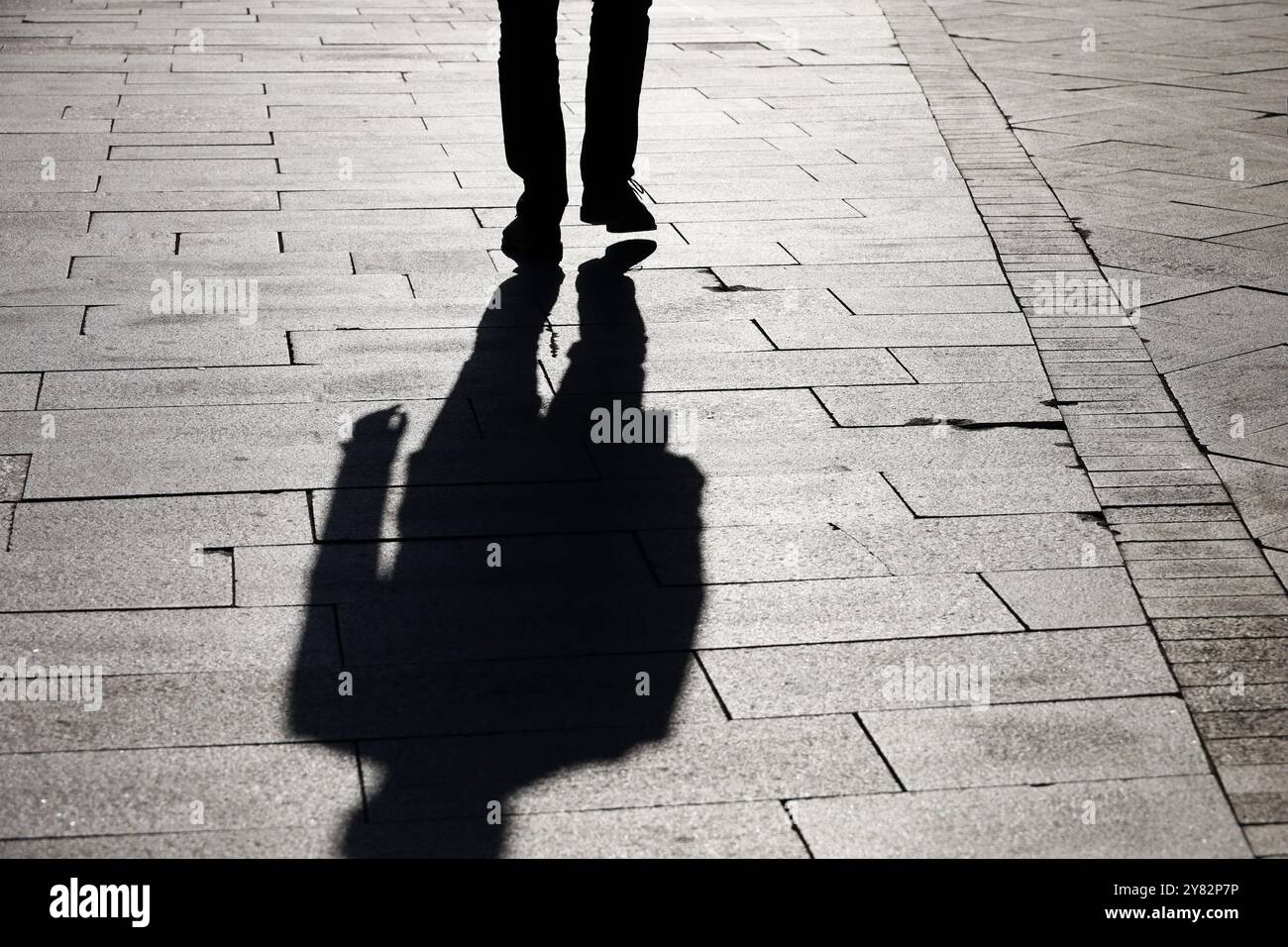 Silhouette noire et ombre d'un homme solitaire marchant dans une rue. Jambes masculines sur le trottoir à l'automne Banque D'Images