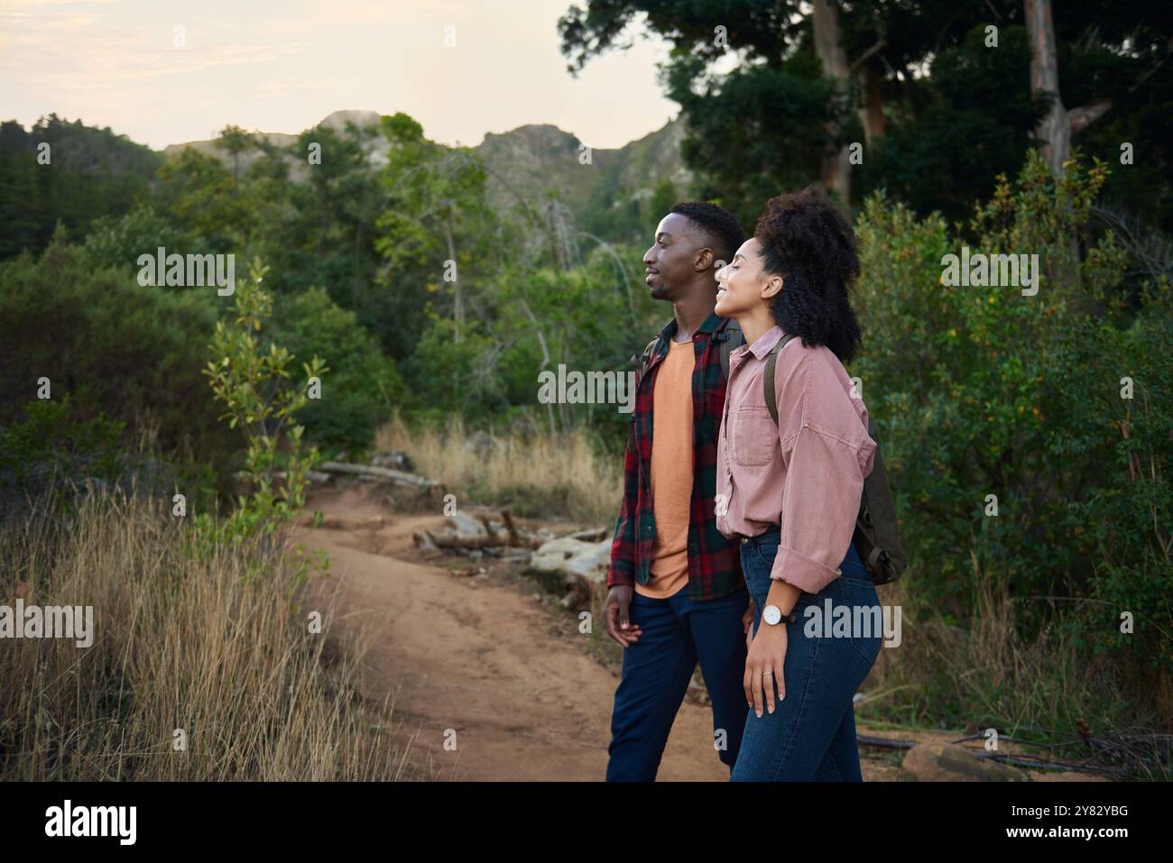 Souriant jeune couple multiethnique regardant la vue panoramique tout en marchant ensemble le long d'un sentier dans quelques collines accidentées en été Banque D'Images
